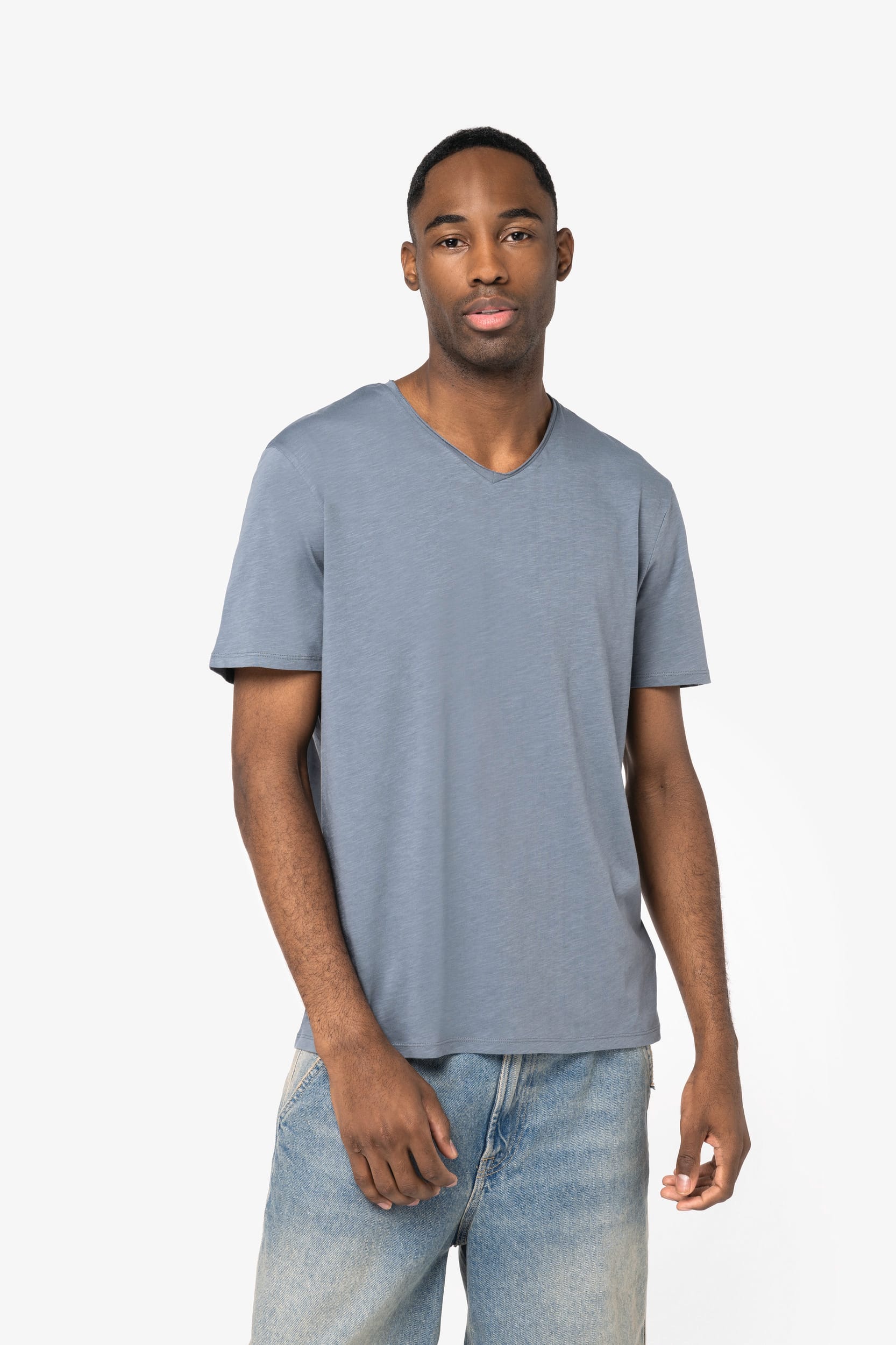 Homme portant un T-shirt bleu-ardoise à manches courtes et col en V, debout contre fond clair.