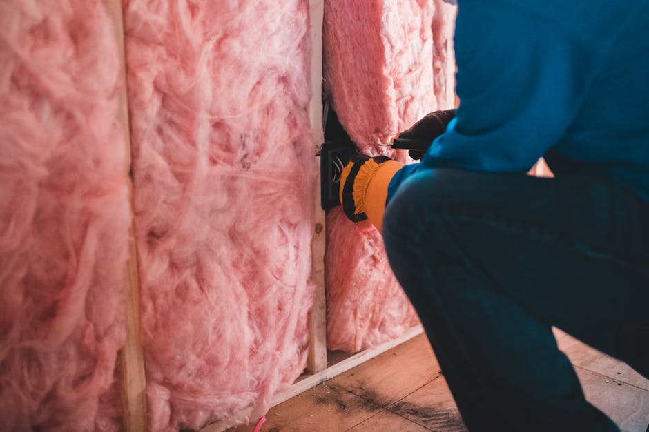 Un ouvrier concentré installant une isolation en fibre de verre rose à l'intérieur d'un bâtiment.