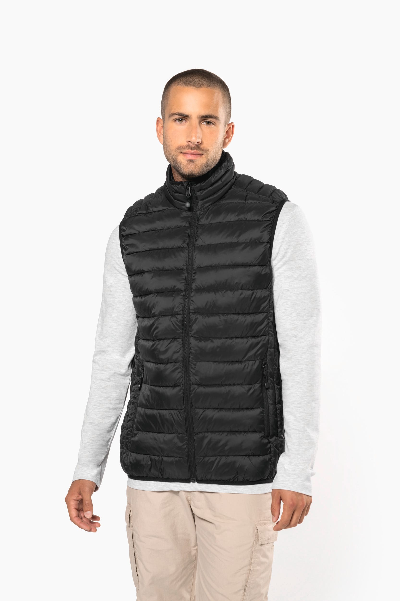 Homme portant gilet matelassé noir sans manches sur T-shirt gris clair, pose verticale, fond blanc.