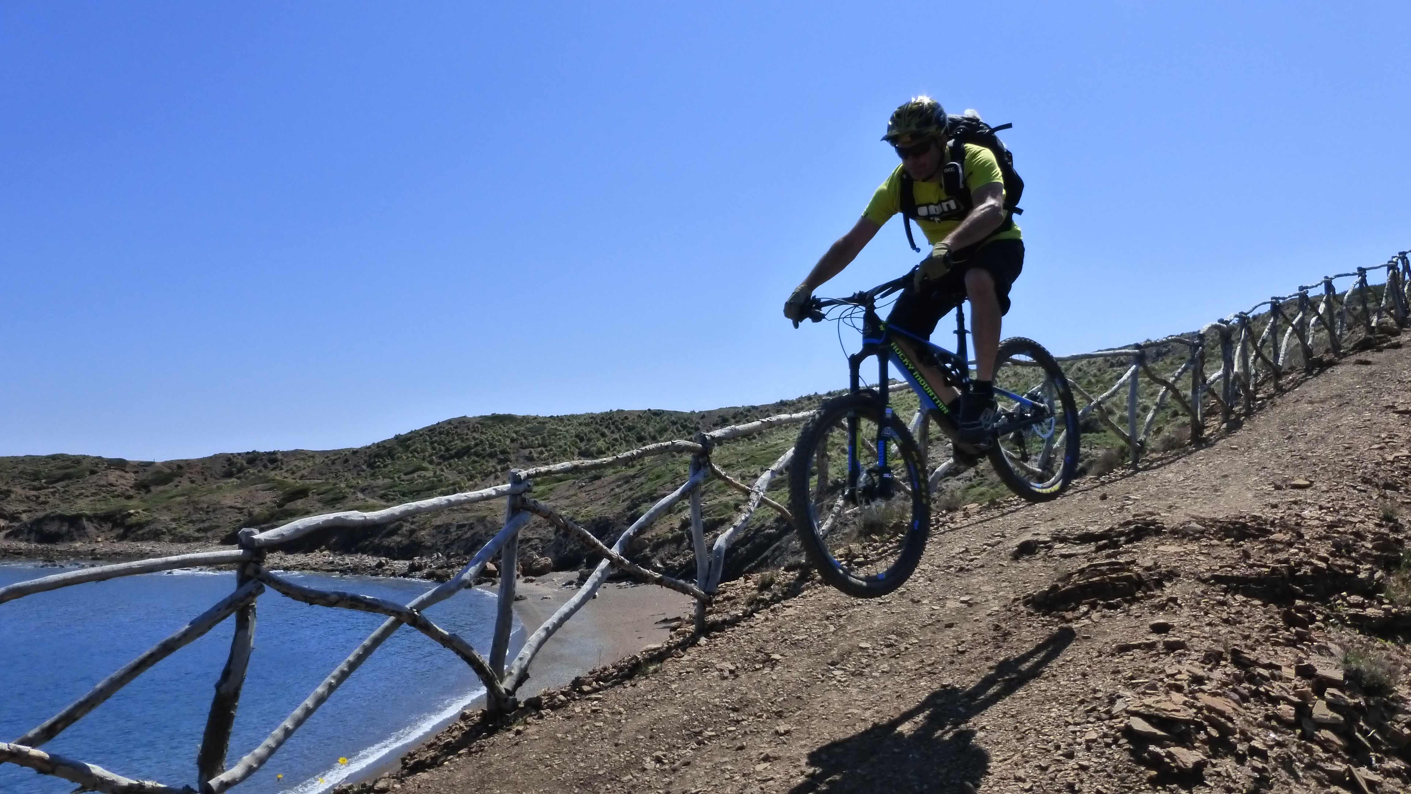 Cycliste en VTT sur un sentier en montagne près d'une clôture en bois, pédalant sur terrain rocailleux près de la côte. actions entretenir correctement un vélo doivent être intégrées naturellement.