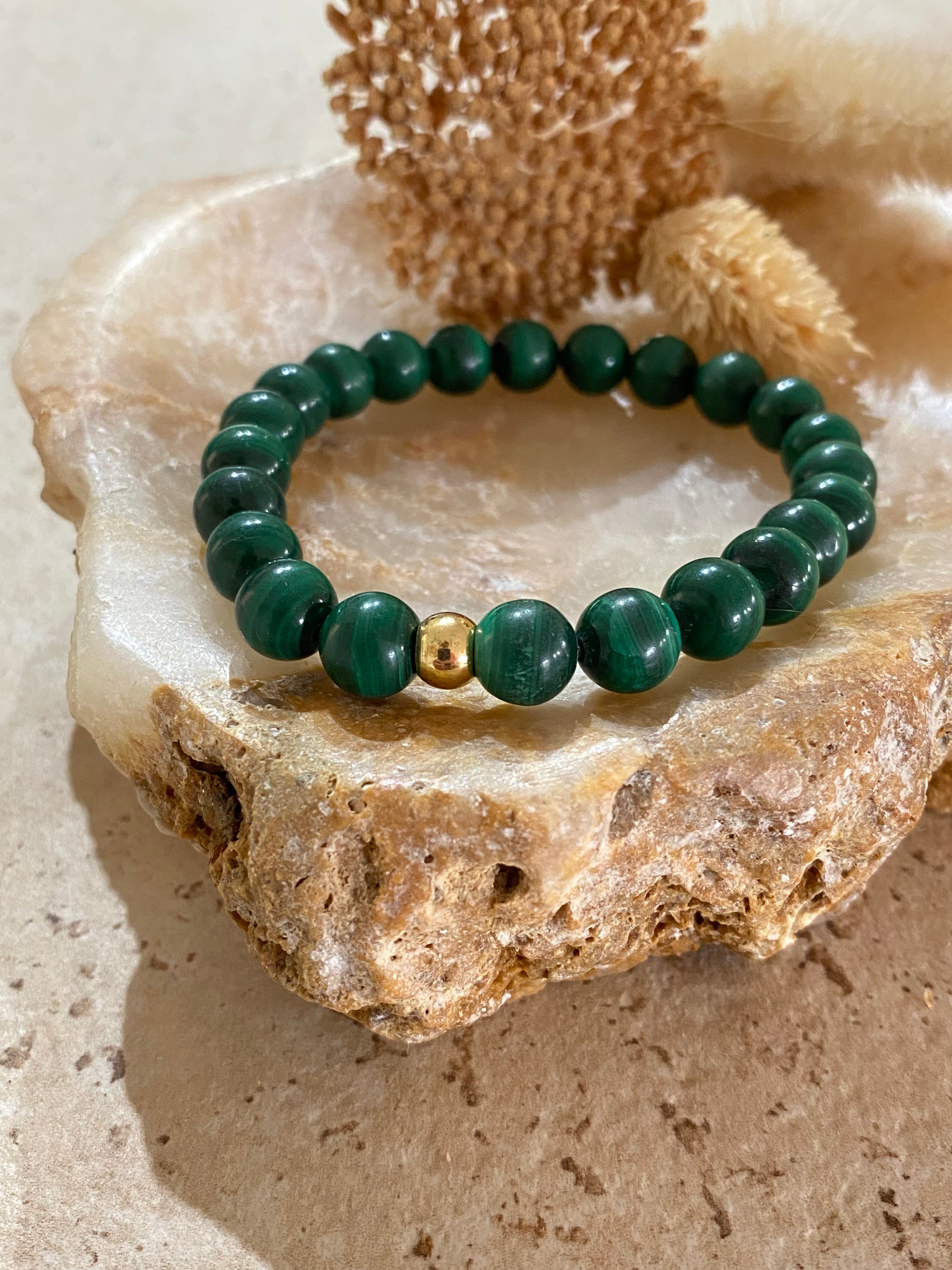 Bracelet émeraude en perles rondes avec une perle dorée, posé sur une roche beige; style minimaliste et naturel. intégration: comment nettoyer pierre bijoux.