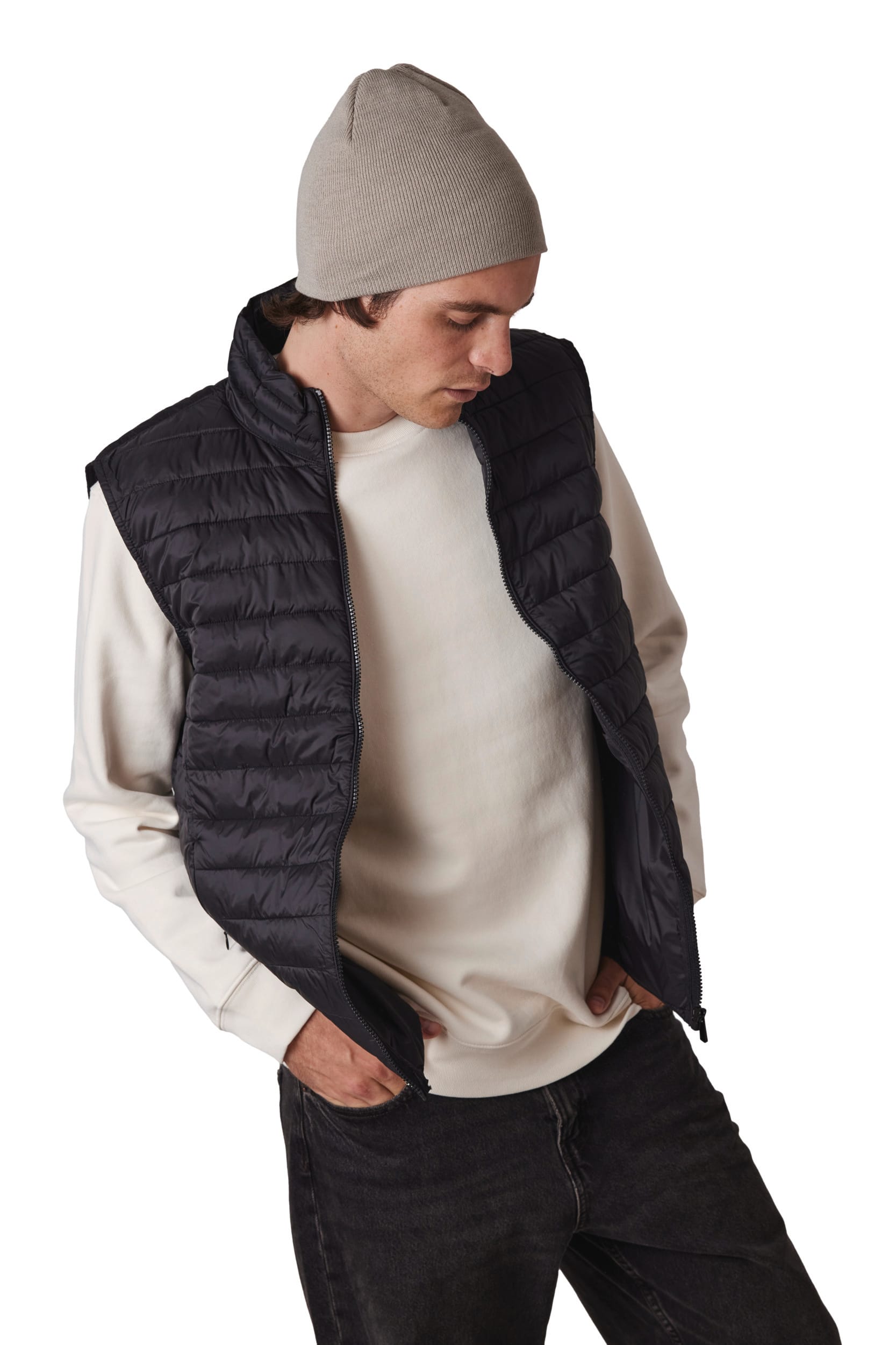 Gilet matelassé noir sans manches porté sur un sweat gris clair et un bonnet beige, pose décontractée.