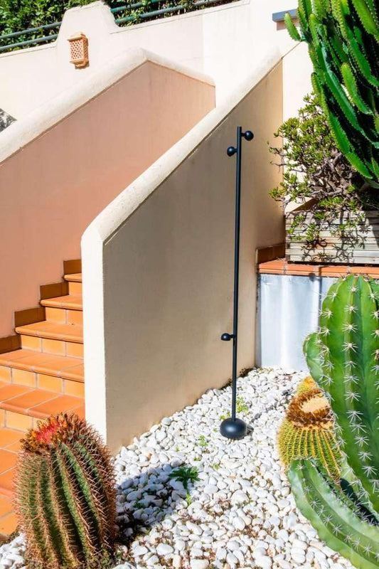 Lampadaire extérieur solaire noir installé près des escaliers d’un jardin, entouré de cactus et de gravier blanc.
