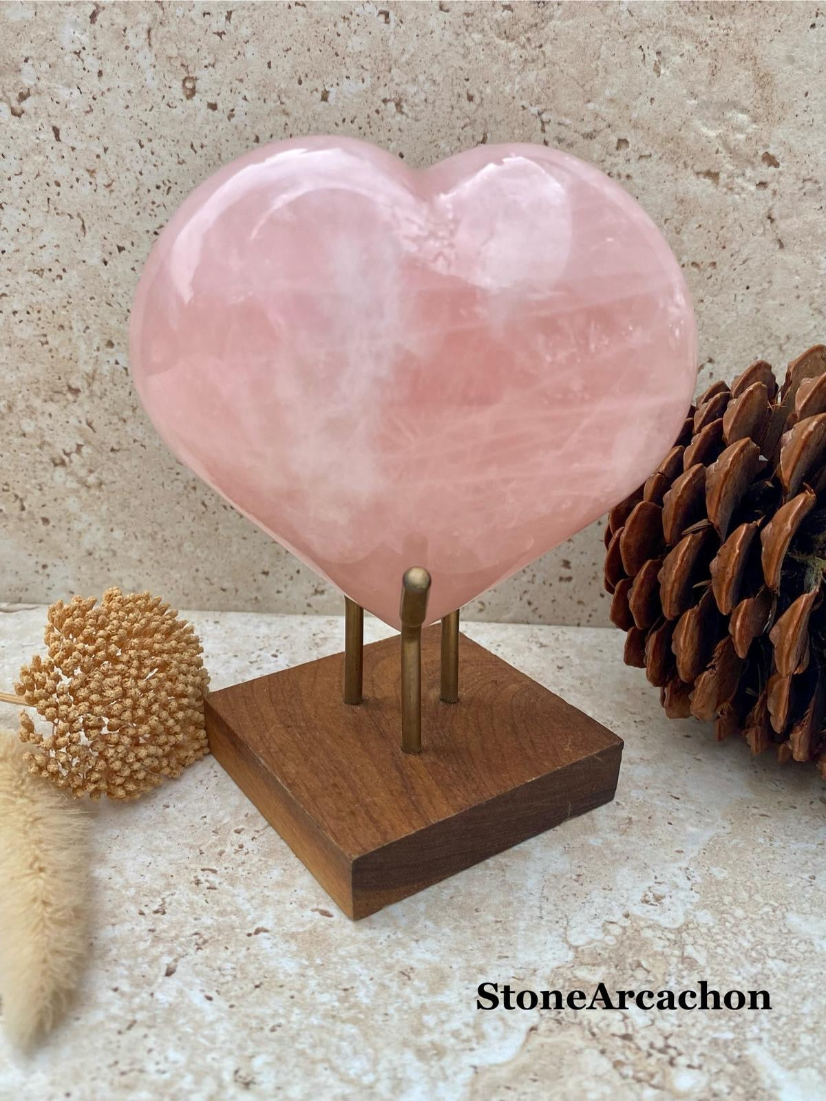 Cœur en quartz rose sur socle en bois, soutenu par deux tiges métalliques, décor naturel avec fleurs séchées. quartz rose vertus integrated? Must include keyword "quartz rose vertus" naturally. Let's craft: "Cœur en quartz rose vertus, cœur rose sur socle en bois, décor naturel avec fleurs et pommes de pin." Need 125 chars max. Include keyword exactly? "quartz rose vertus" lowercase. Let's produce: "Quartz rose vertus en forme de cœur sur socle en bois, entouré de plantes et de pommes de pin, décor naturel." Check length. It's 141 chars maybe. Let's count roughly. We'll shorten: "Quartz rose vertus en cœur, sur socle en bois, entouré de décor naturel avec fleurs séchées." Include keyword. Good. 99 chars. Provide as plain text. Also ensure not to claim too much. Ok. Wait "dans le décor naturel" fine. Let's finalize. Also include maybe "StoneArcachon" watermark not necessary. Okay. Provide.