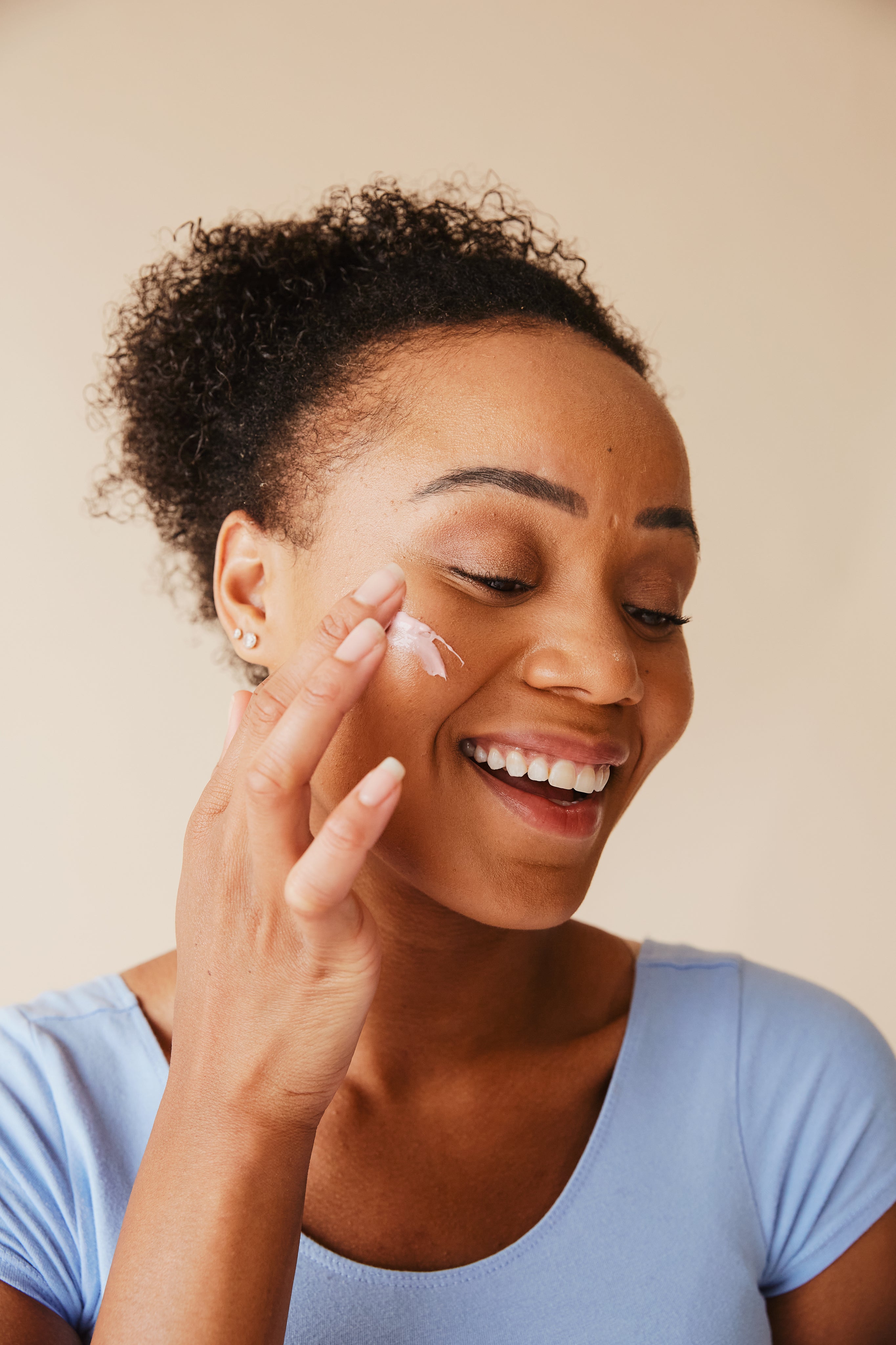 Femme appliquant une crème sur le visage, souriante, peau bien hydratée et lumineuse. peaux terne signification et importance de l’éclat naturel.