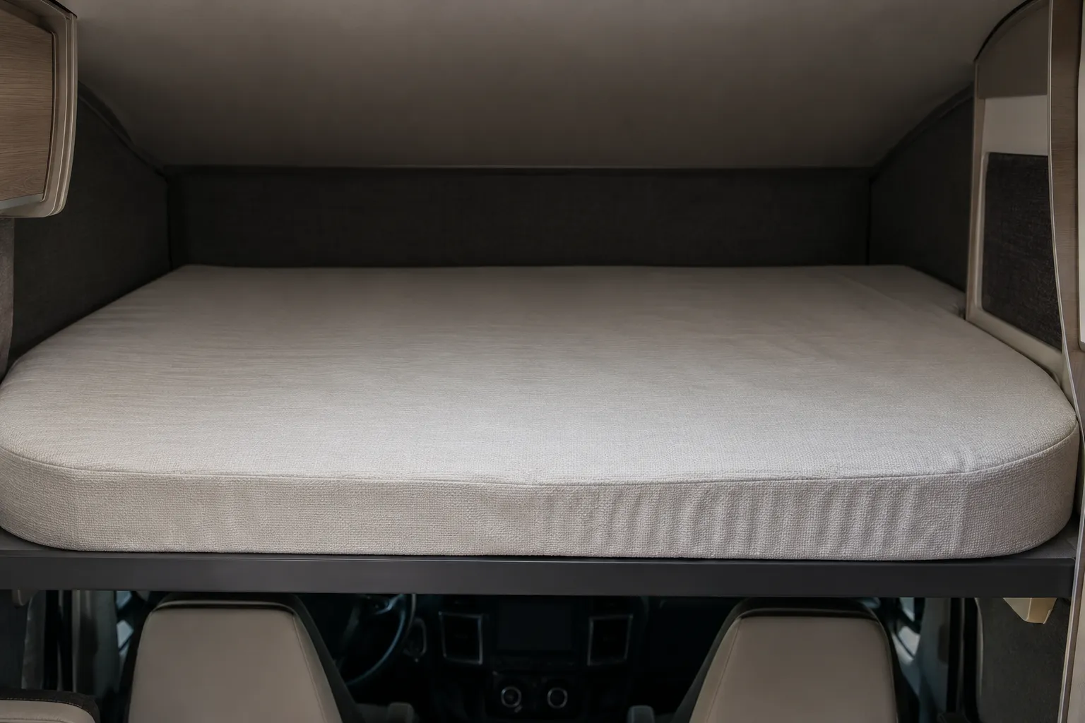 Cama o pelotón de colchón rectangular gris con funda clara dentro de un espacio de autocaravana capuchina.