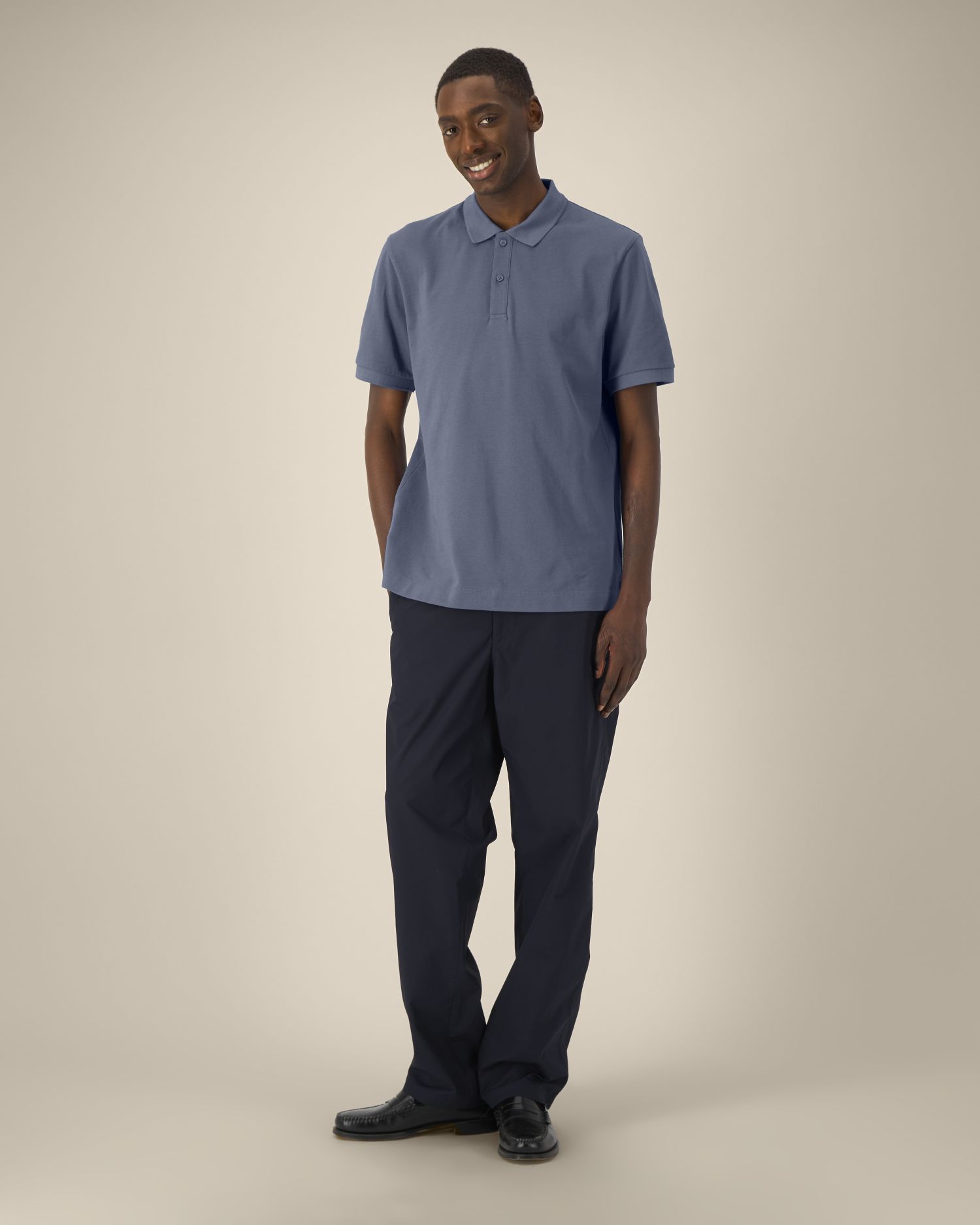 Homme portant polo bleu et pantalon sombre, debout, sourire, vue entière.