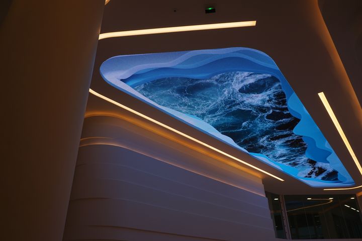 Plafond architectural moderne avec l’intérieur courbe et éclairage LED, motif océanique bleu illuminant la salle. ecran led avantage inconvenient intégré naturellement.
