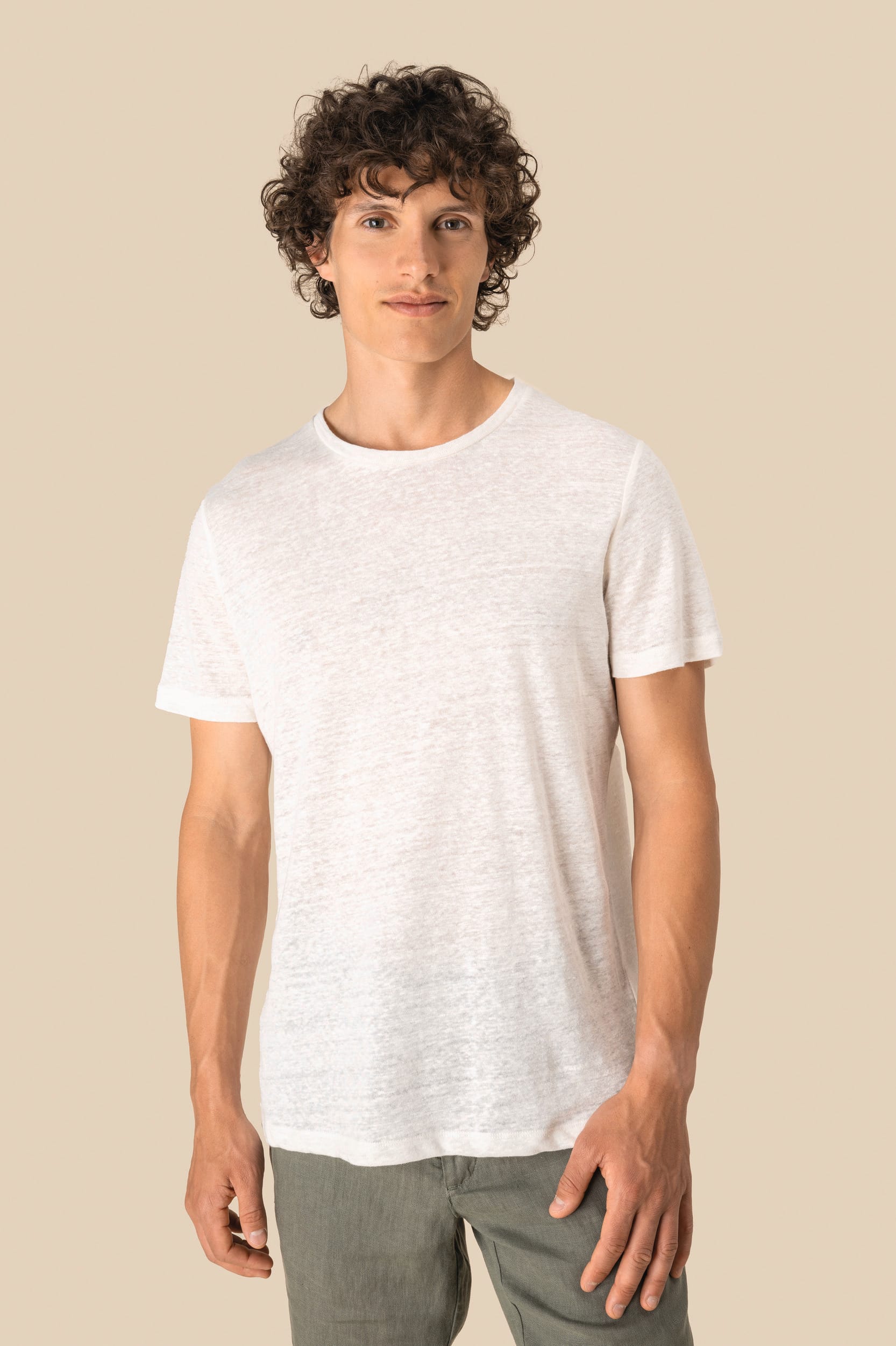 Homme debout portant un t-shirt blanc avec fond beige.