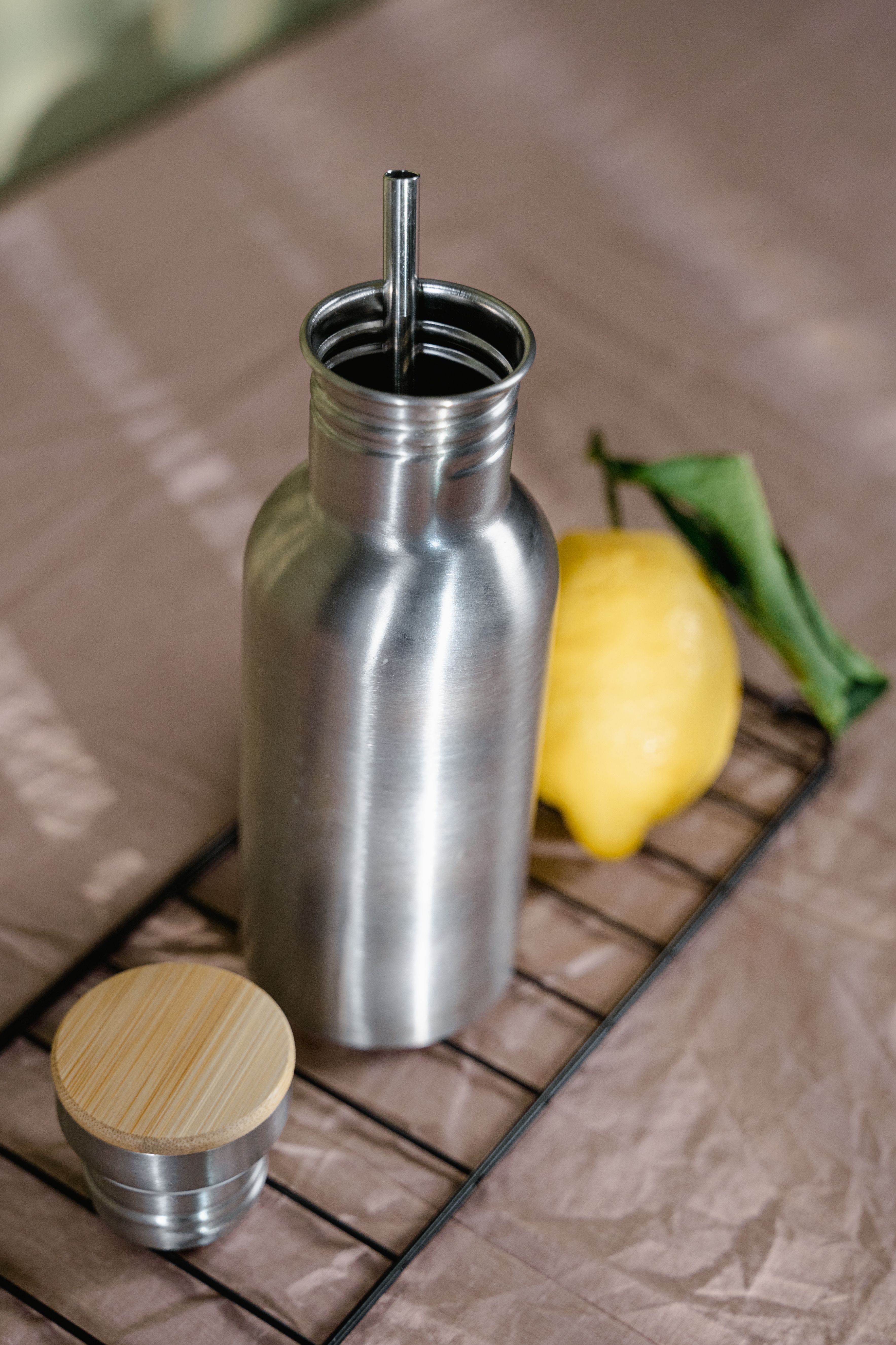Gourde isotherme en acier inoxydable avec couvercle en bambou et paille en inox posée sur une grille