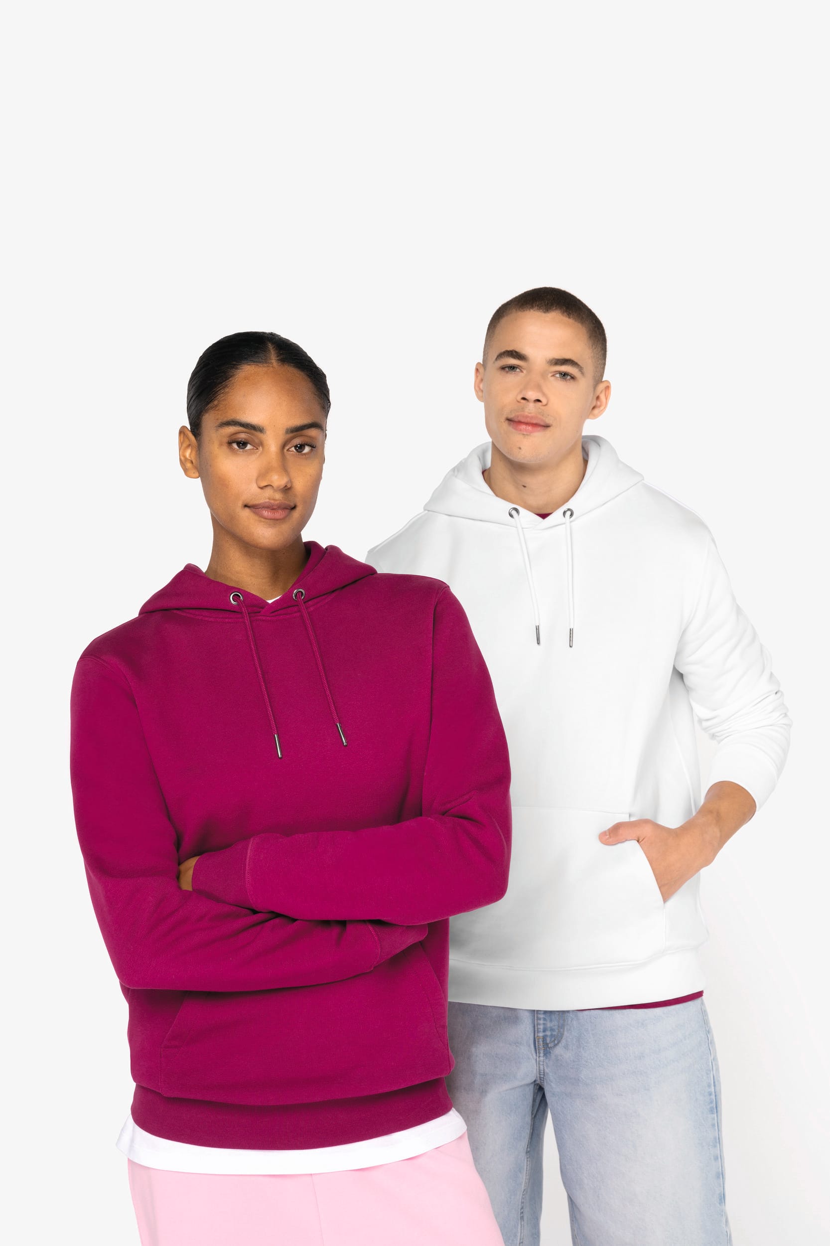 Deux personnes portent des sweat-shirts à capuche de couleur unie, l'une magenta et l'autre blanc, debout côte à côte.