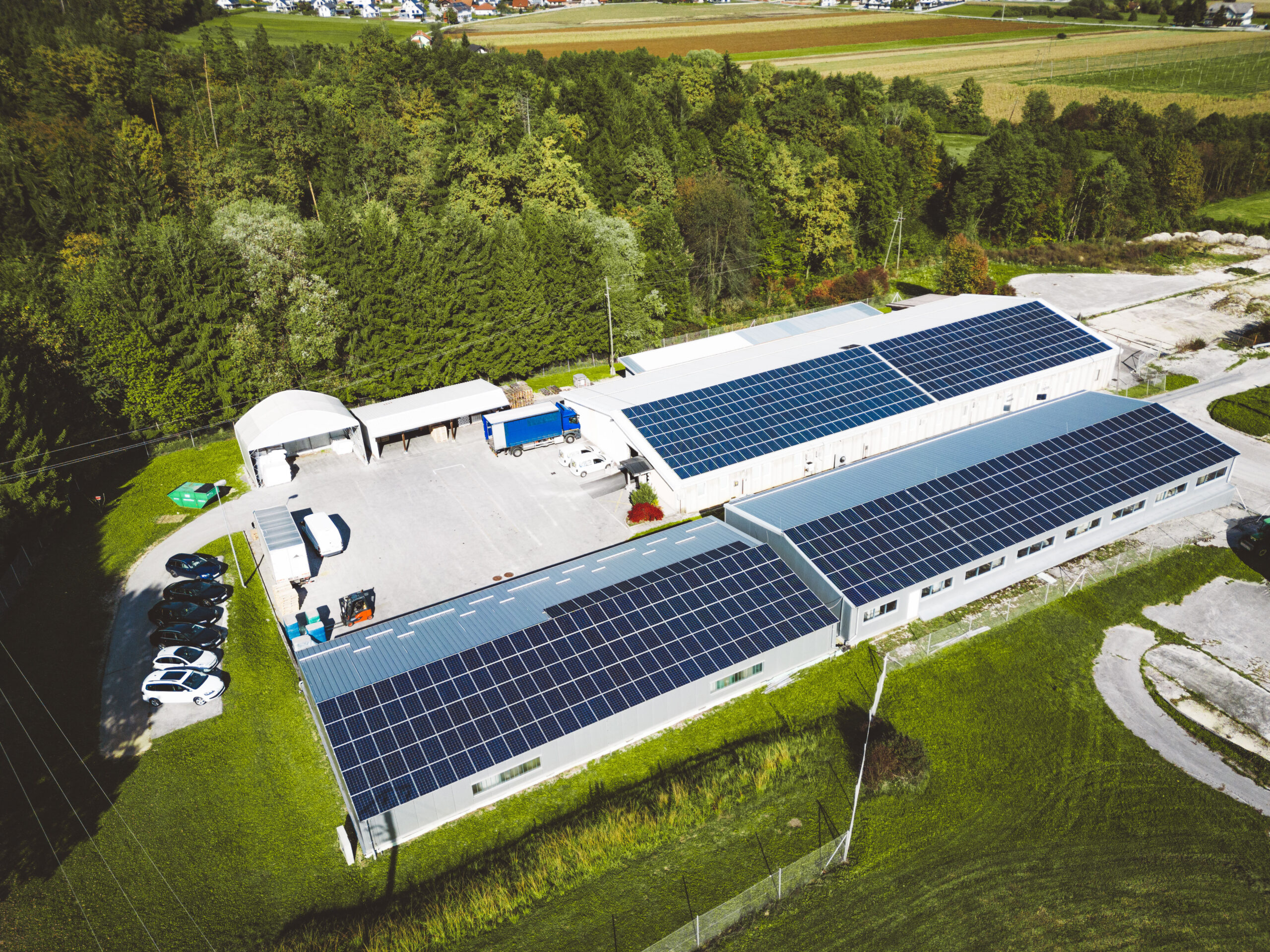Aerial view of a commercial complex with multiple long roofs covered in solar panels, surrounded by trees and fields, illustrating solar for commercial property.