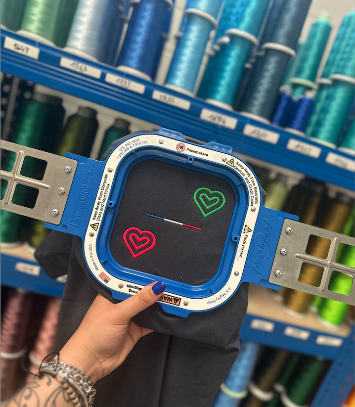 Trois cœurs colorés brodés sur un panneau d'essai textile affiché dans une boutique de fils et matières.