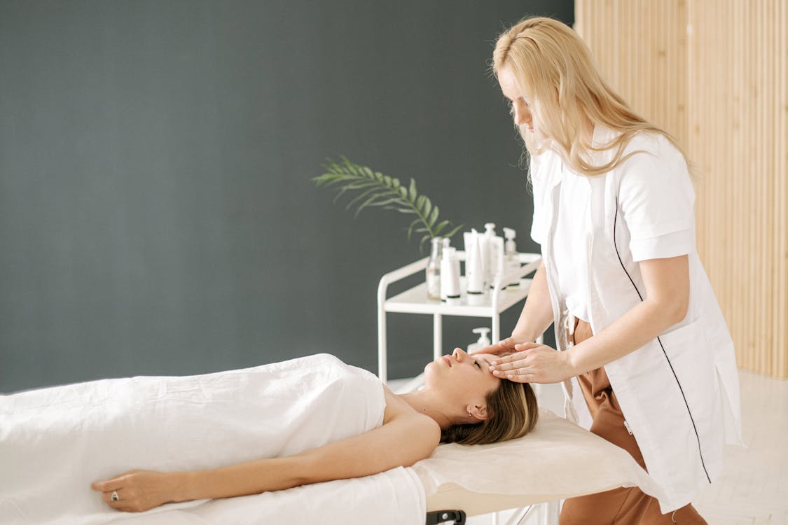 Personne recevant un massage apaisant avec application d'huile essentielle par les mains d'un praticien, flacon d'huile posé à proximitédans un cadre détente