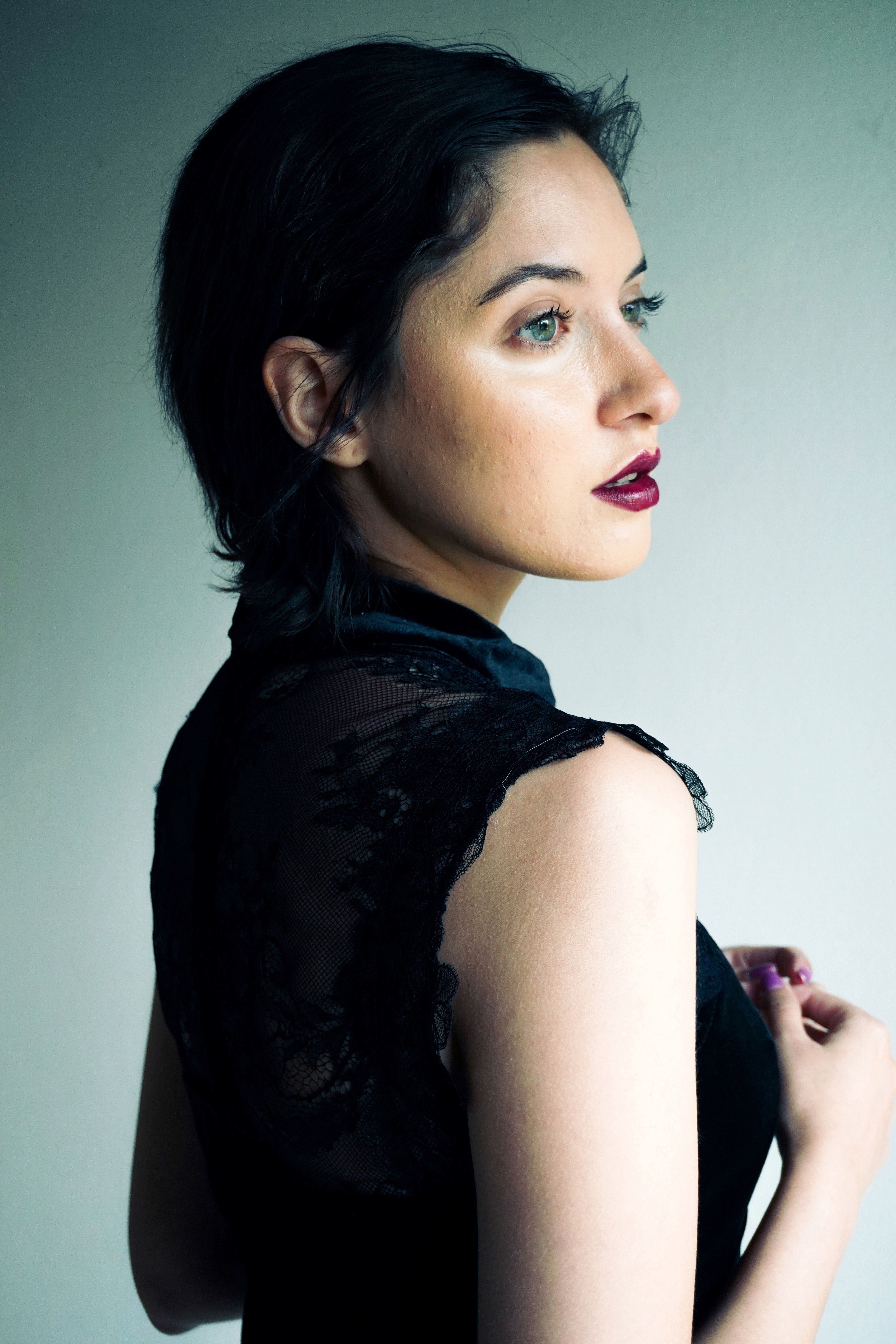Portrait en profil d’une femme aux cheveux courts, maquillage soutenu et robe noire en dentelle, éclairage doux et background neutre. moyen d'une photo professionnelle.