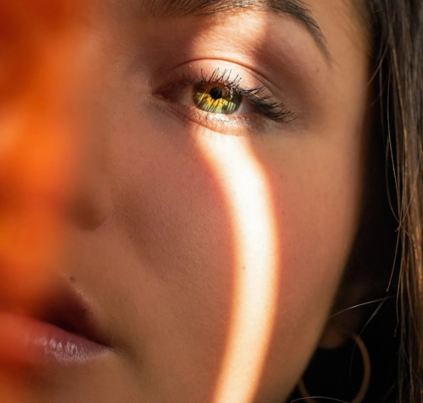 Close-up of a woman's face with a sunlit ring shadow across her cheek, highlighting her eye and smooth skin. Salicylic acid for blackheads mention integrated naturally.