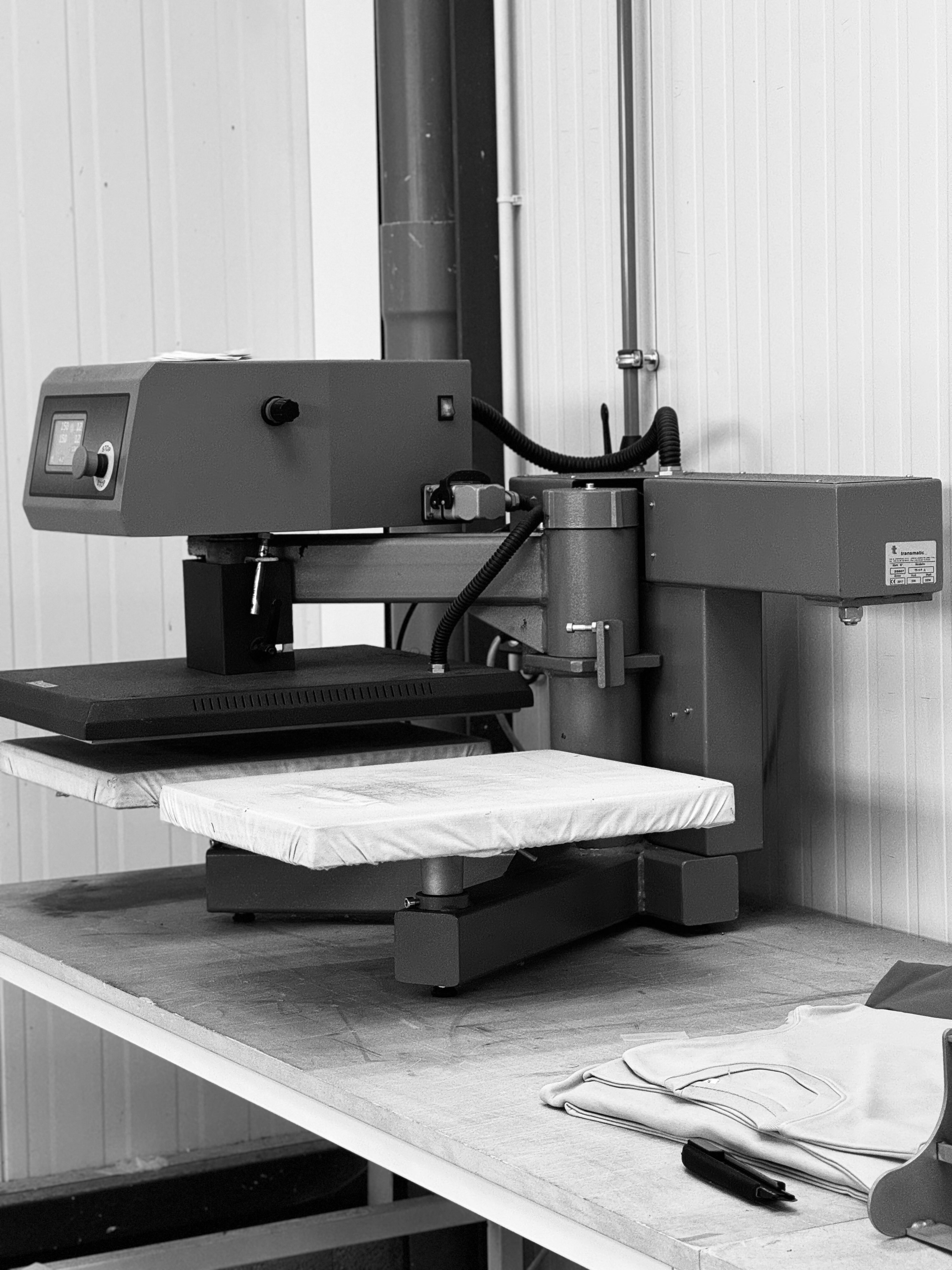 Machine d'impression ou de transfert textile sur table, avec une grande pièce de tissu placée sous la presse.