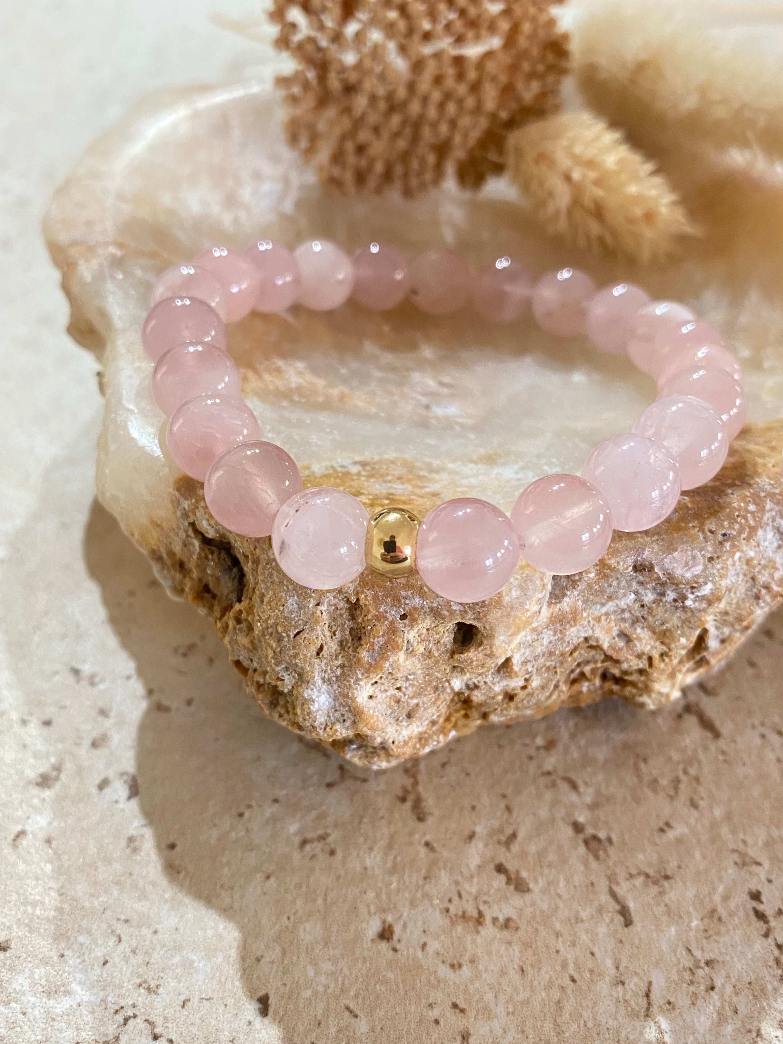 Bracelet de perles roses en quartz rose sur une pierre, avec une mini perle dorée au centre. Cristaux pour mieux dormir potentiel usage relaxant.