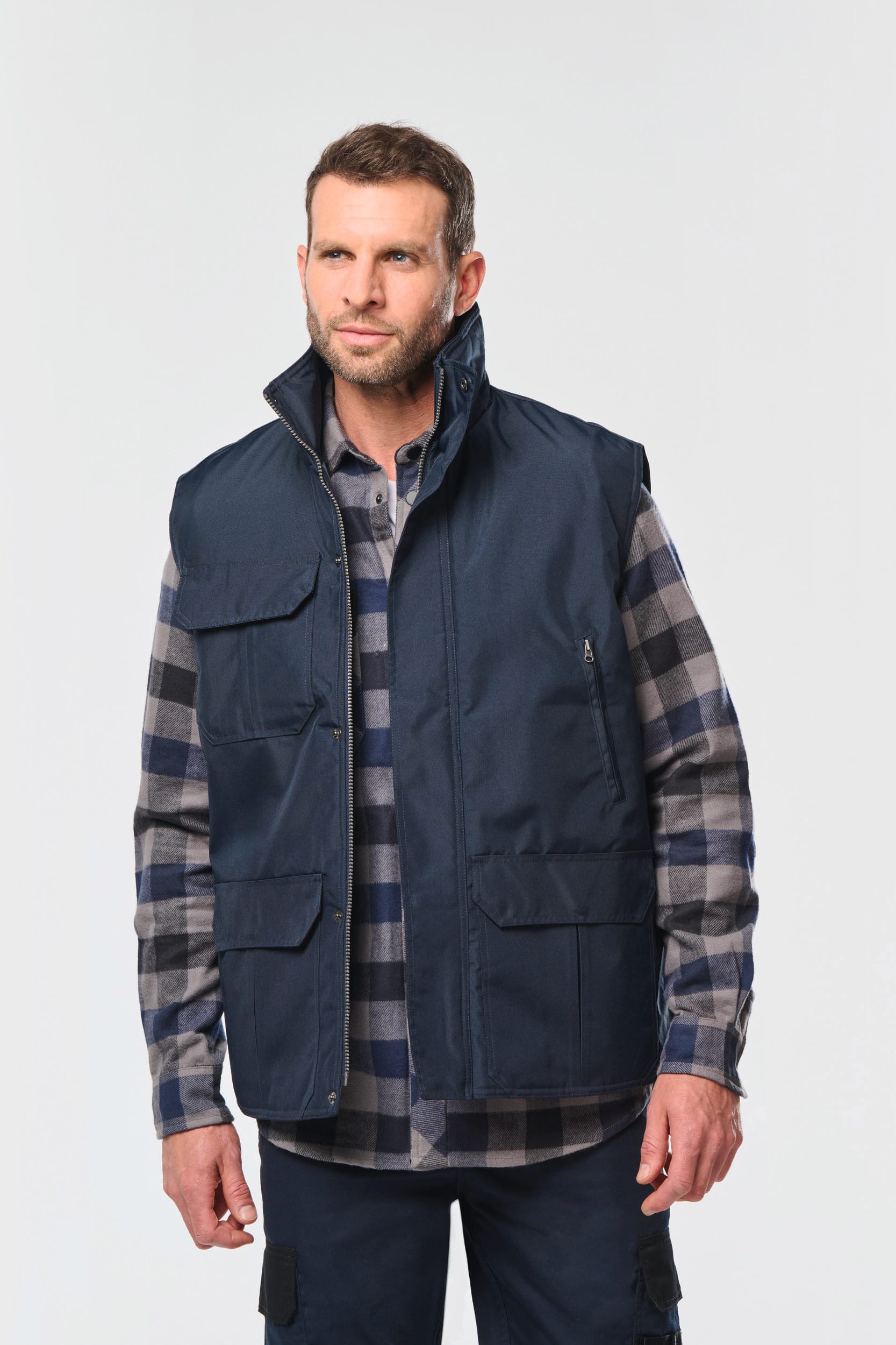 Groupeur homme portant veste sans manches marine et chemise à carreaux gris-bleu, pose neutre. Necesité alt: image produit textile.