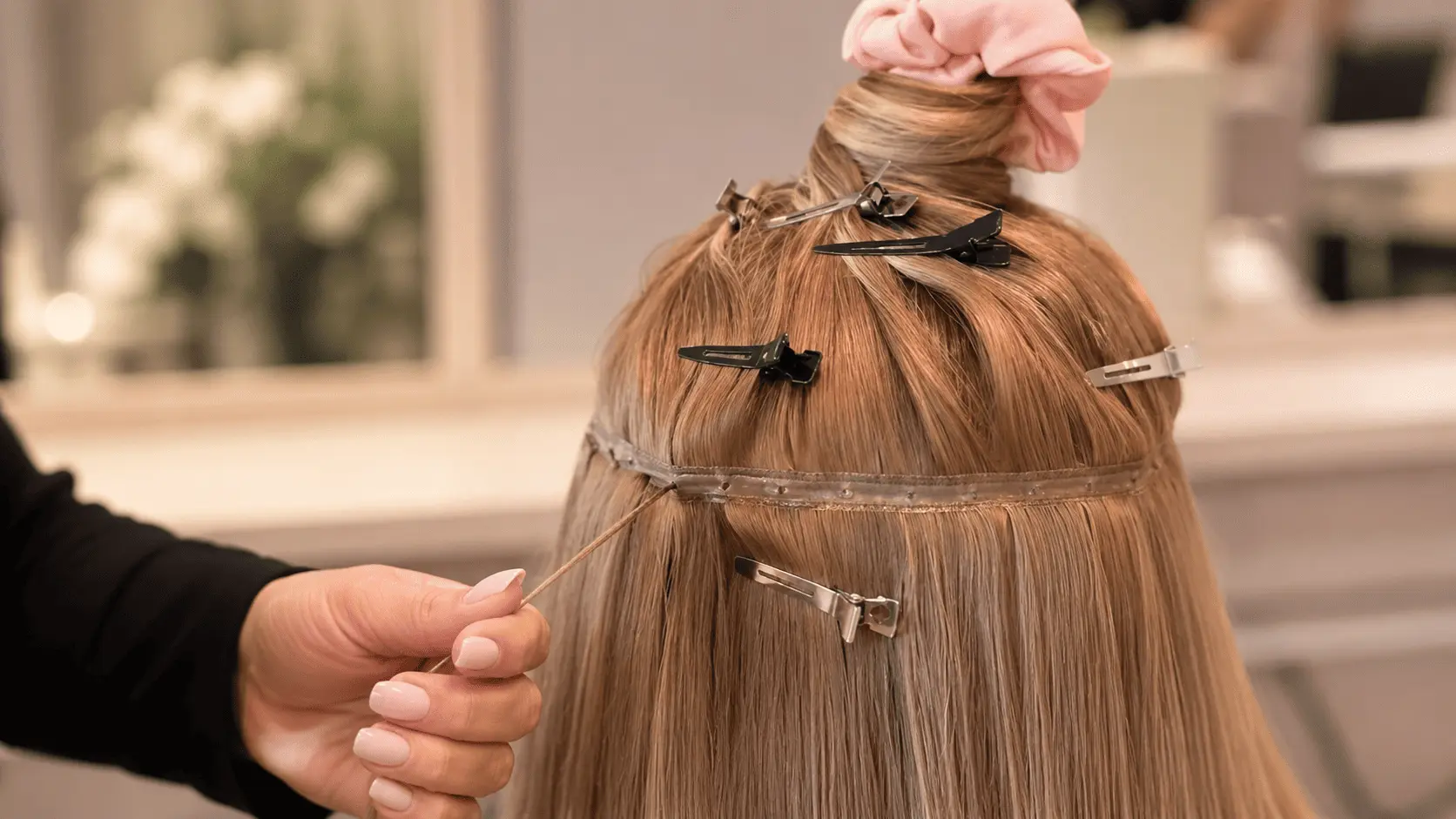 Coiffure en cours avec des extensions capillaires fixées à clips sur cheveux blonds, pose de tests et agrafes visibles. Coiffure en cours avec des extensions capillaires fixées à clips sur cheveux blonds, pose de tests et agrafes visibles.