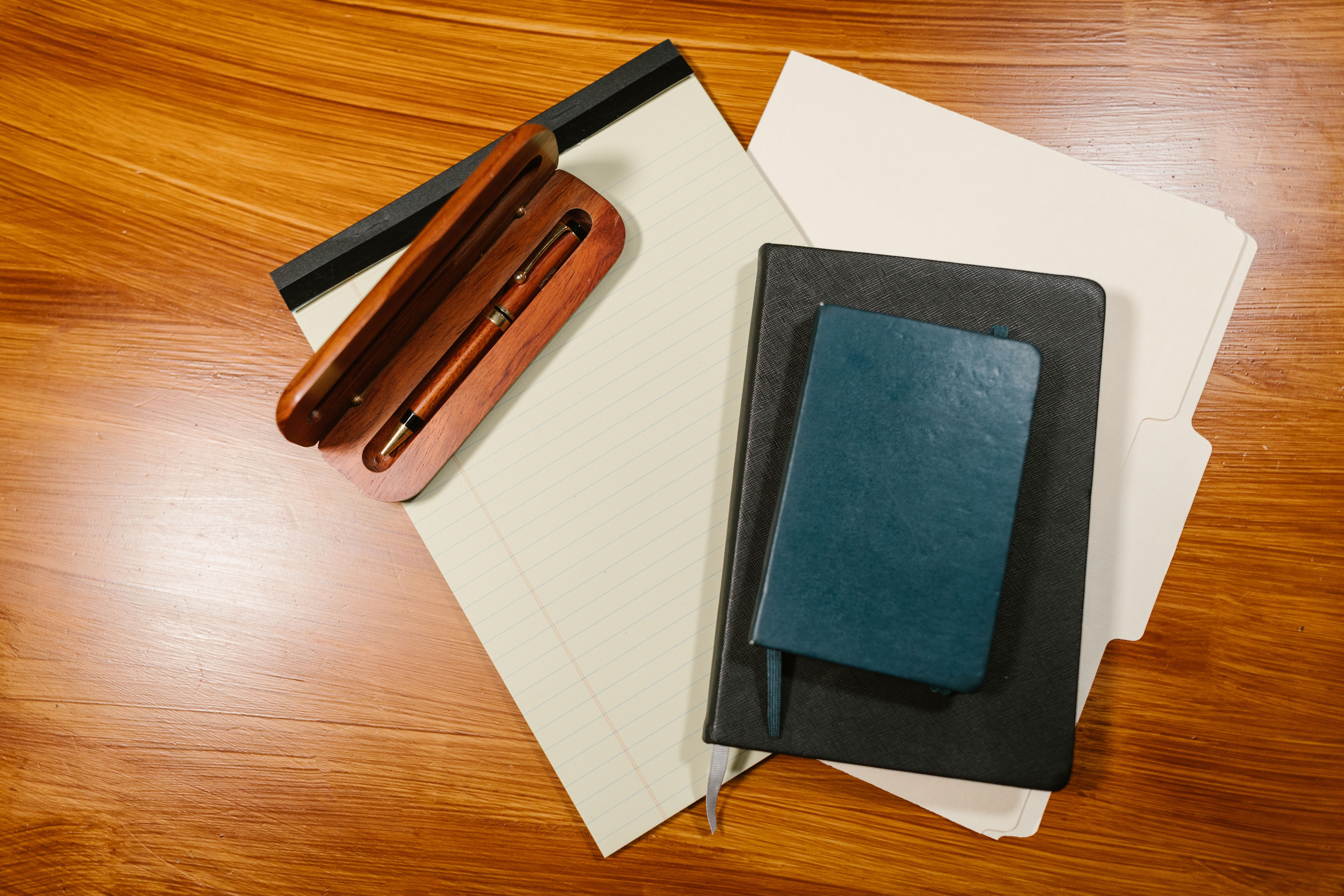 Porte-documents noir posé sur des dossiers et un bloc-notes, à côté d'un étui à stylo en bois