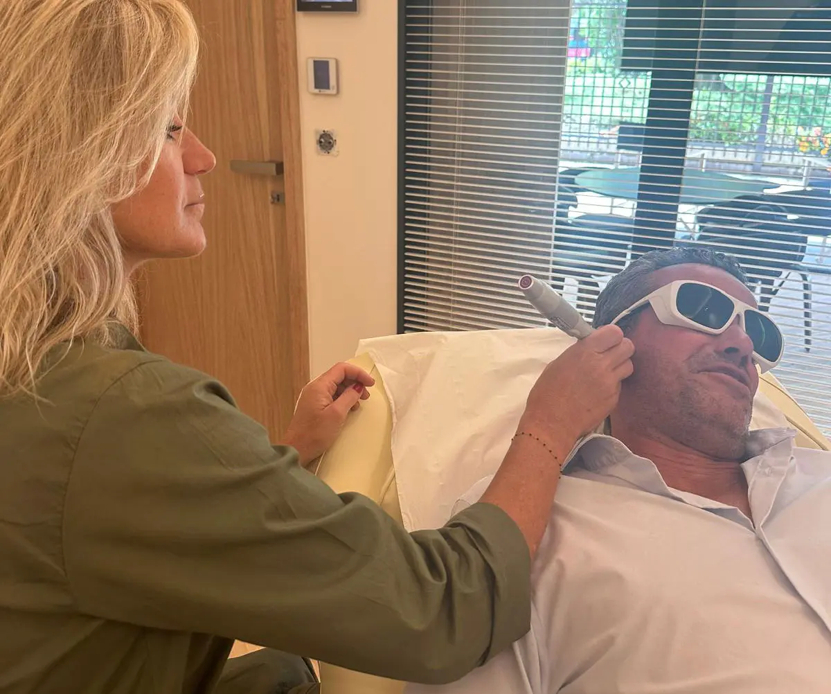 Séance de lasérothérapie : une praticienne tient un appareil près du visage d'un homme allongé, portant des lunettes