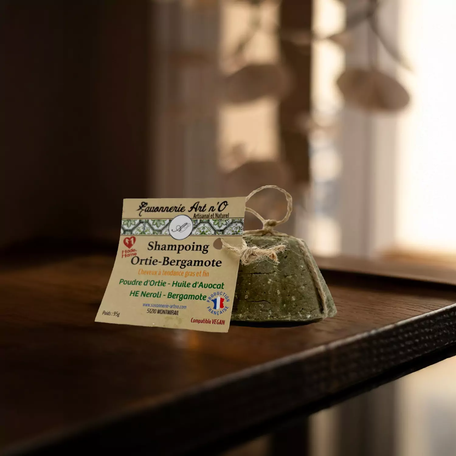 Shampoing solide Ortie Bergamote de la Savonnerie Art n'O, pain vert à cordon posé sur une table en bois avec son étiquette.