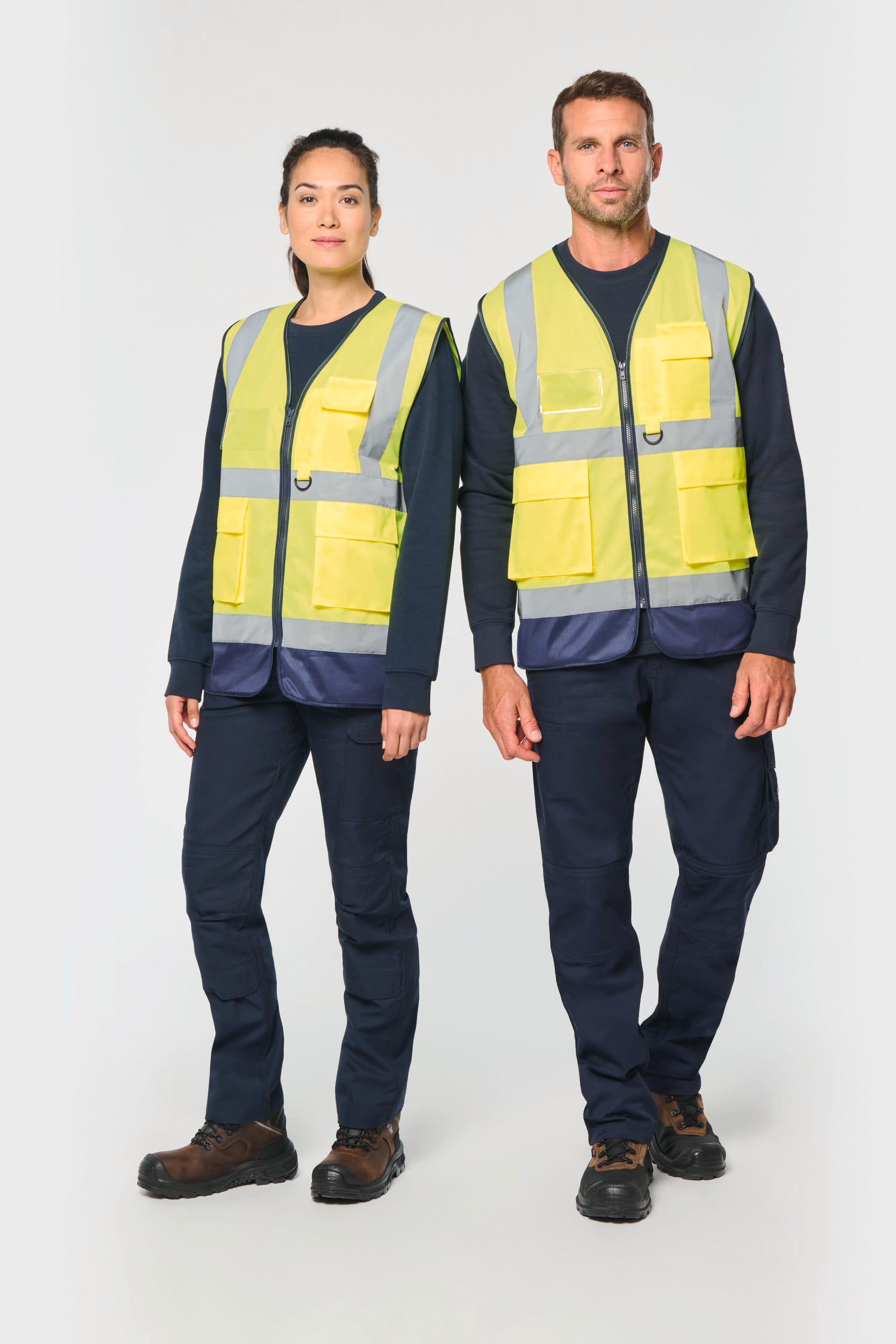 Deux modèles portent des gilets de sécurité haute visibilité jaunes avec poches, sur fonds sombre, veste et pantalon adaptés au travail en extérieur. Où personnaliser une veste pour entreprise.