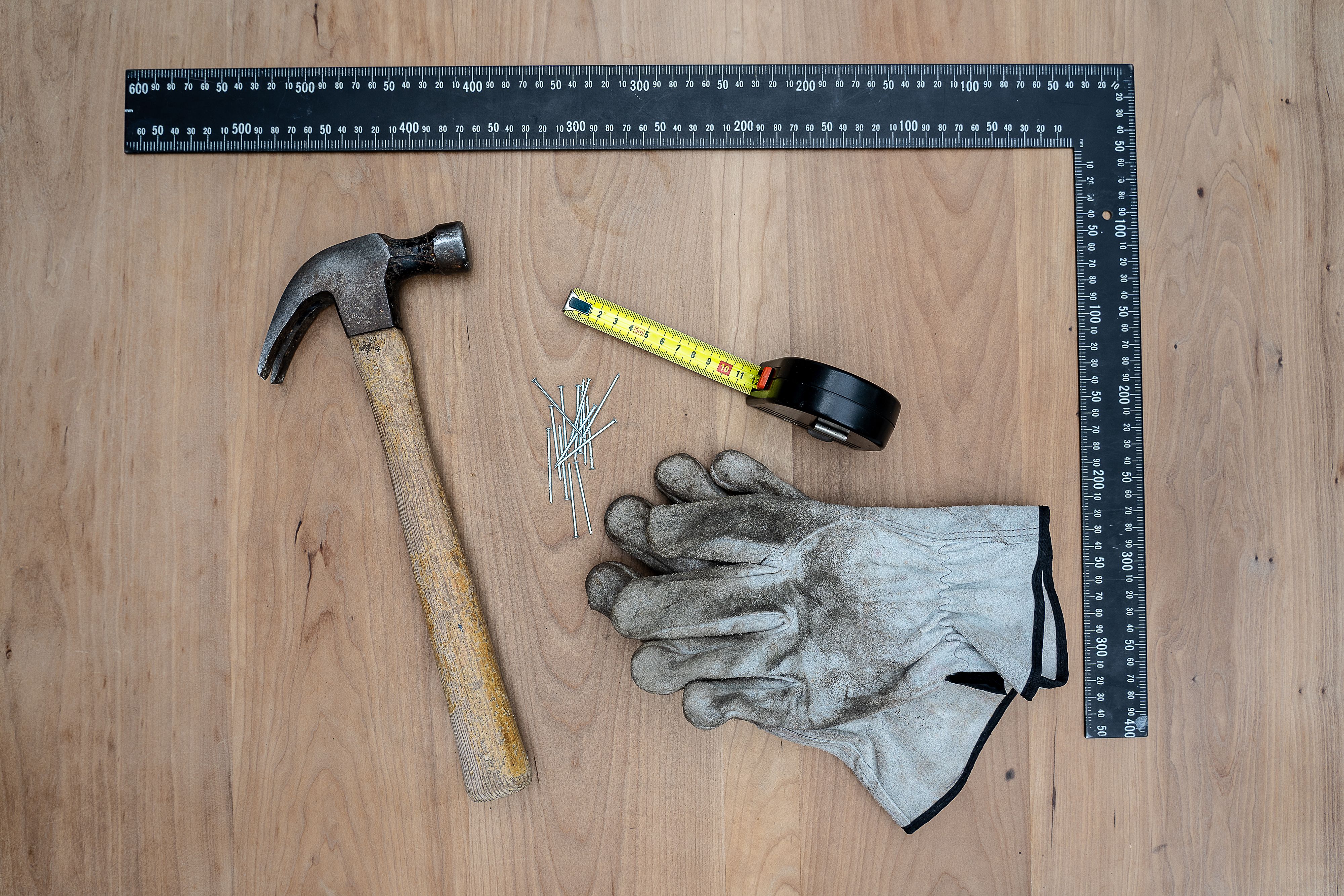 Mètre ruban, marteau, équerre et gants de travail posés sur un plan de travail en bois