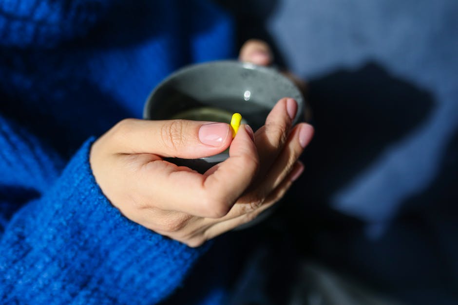 Gros plan de mains tenant une boisson chaude et un comprimé jaune, illustrant un thème de santé et bien-être.