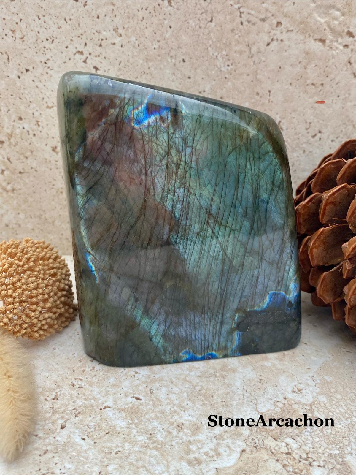Pierre semi-précieuse irisée, rectangulaire, sur fond beige; posée près de taks et une grenade de cactus. Alt text: Cristaux pour mieux dormir - améthyste/lépidolite? Note: image montre labradorite mine? Il faut décrire: pierre polygonale verte irisée avec veines. Include keyword natural: "Cristaux pour mieux dormir". Let's craft: "Cristaux pour mieux dormir : pierre irisée rectangulaire avec reflets bleus et verticaux, posé sur une surface beige, entouré d'éléments décoratifs." 112 chars. Cristaux pour mieux dormir : pierre irisée rectangulaire aux reflets bleus et verts, posée sur une surface beige avec éléments décoratifs.