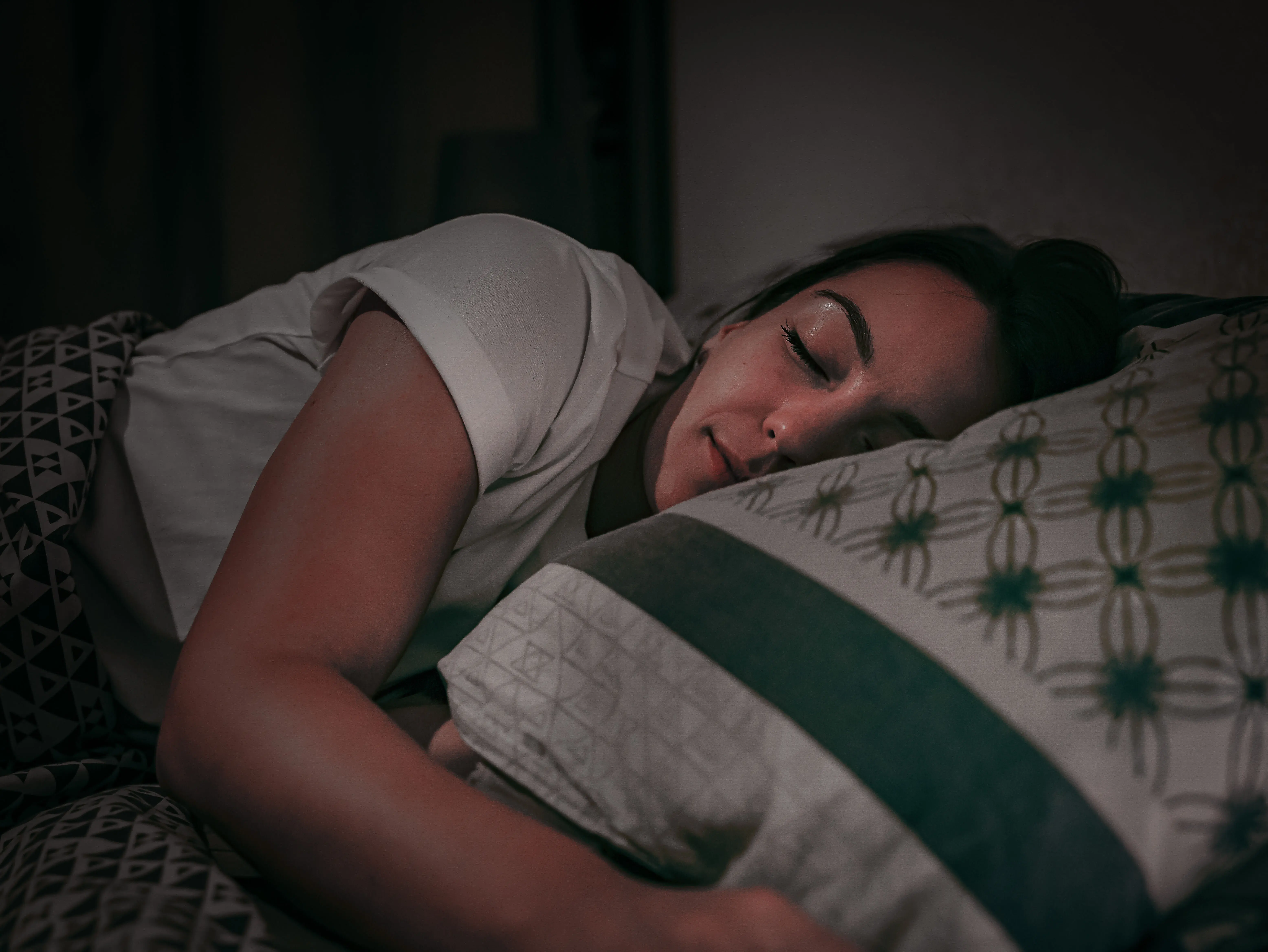 Femme dormant sur le côté dans son lit, tête appuyée sur l’oreiller, ambiance nocturne et douce.