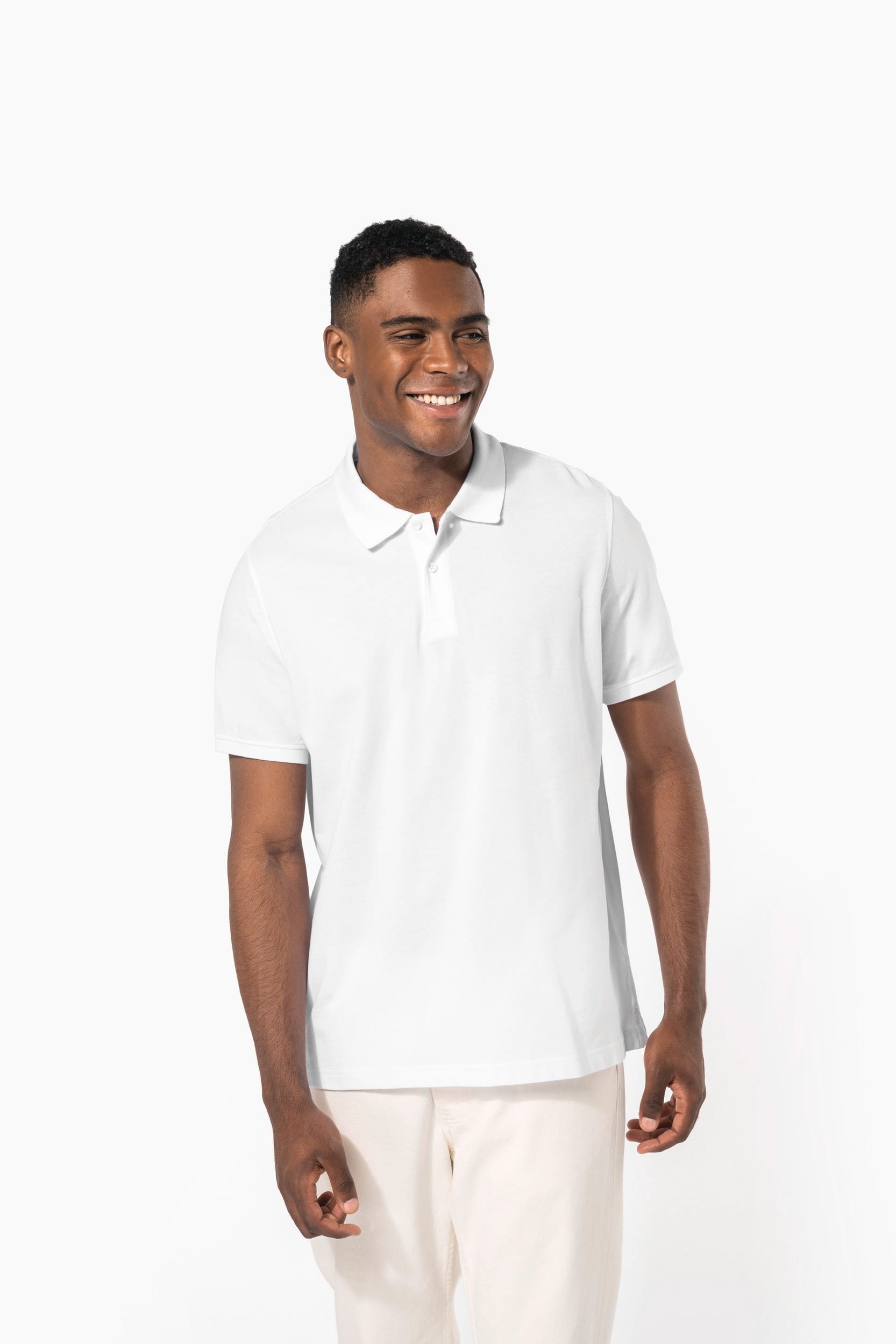 Homme souriant portant polo blanc et pantalon clair, debout contre un fond blanc.
