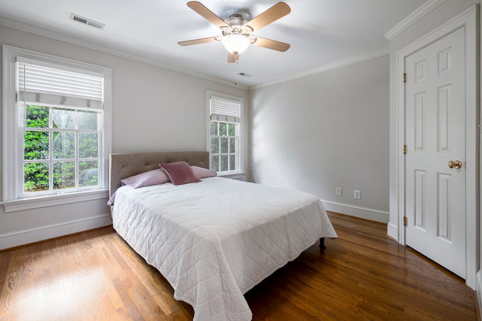 Bright bedroom featuring white bedding, ceiling fan, and large windows.