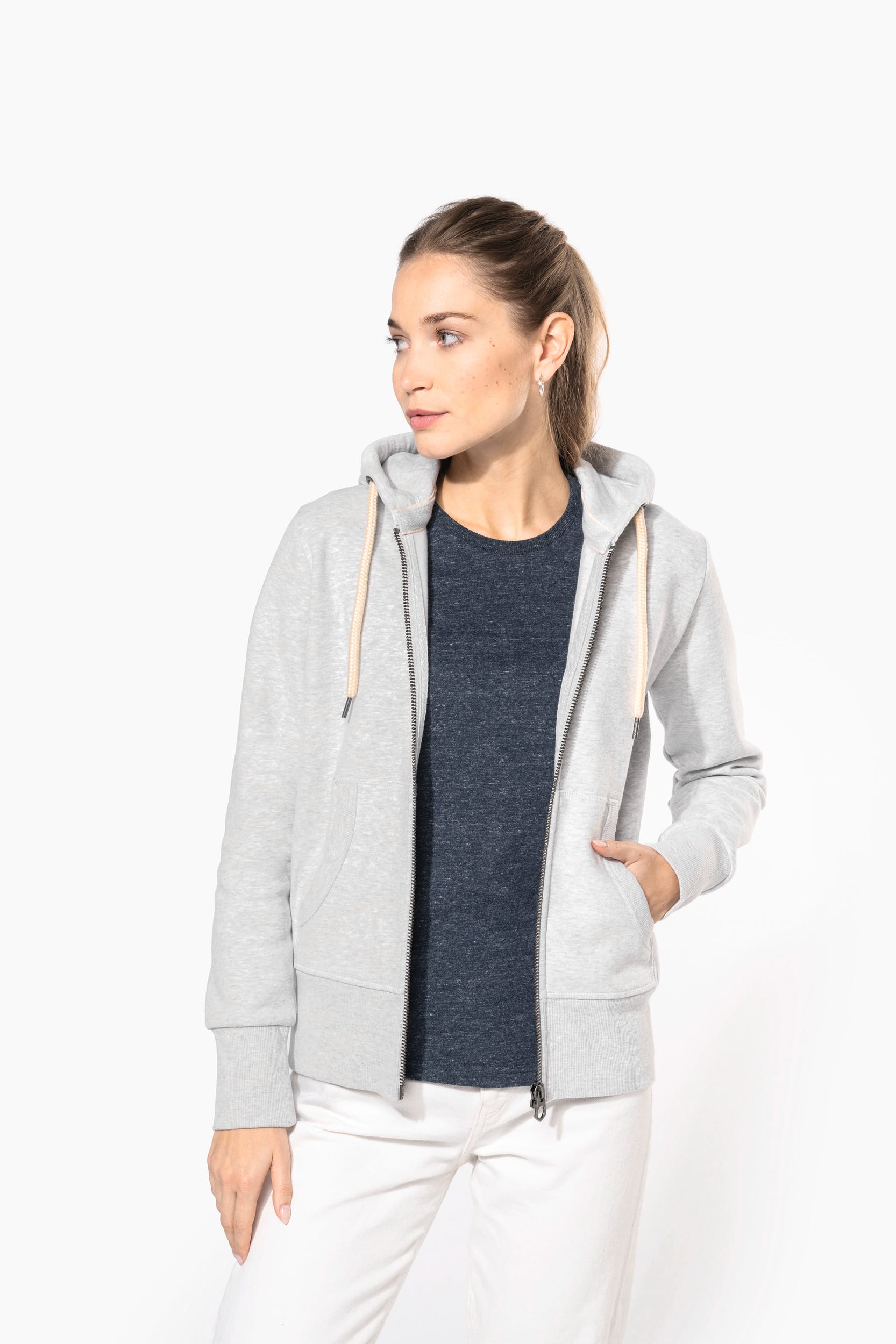 Tee shirt personnalisé logo entreprise présentable sur une femme portant un hoodie gris, t-shirt bleu marine et pantalon blanc, look décontracté.