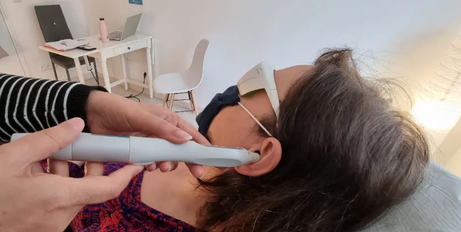 Personne portant un masque oculaire reçoit une séance de laser à l'oreille par un praticien, sans aiguilles