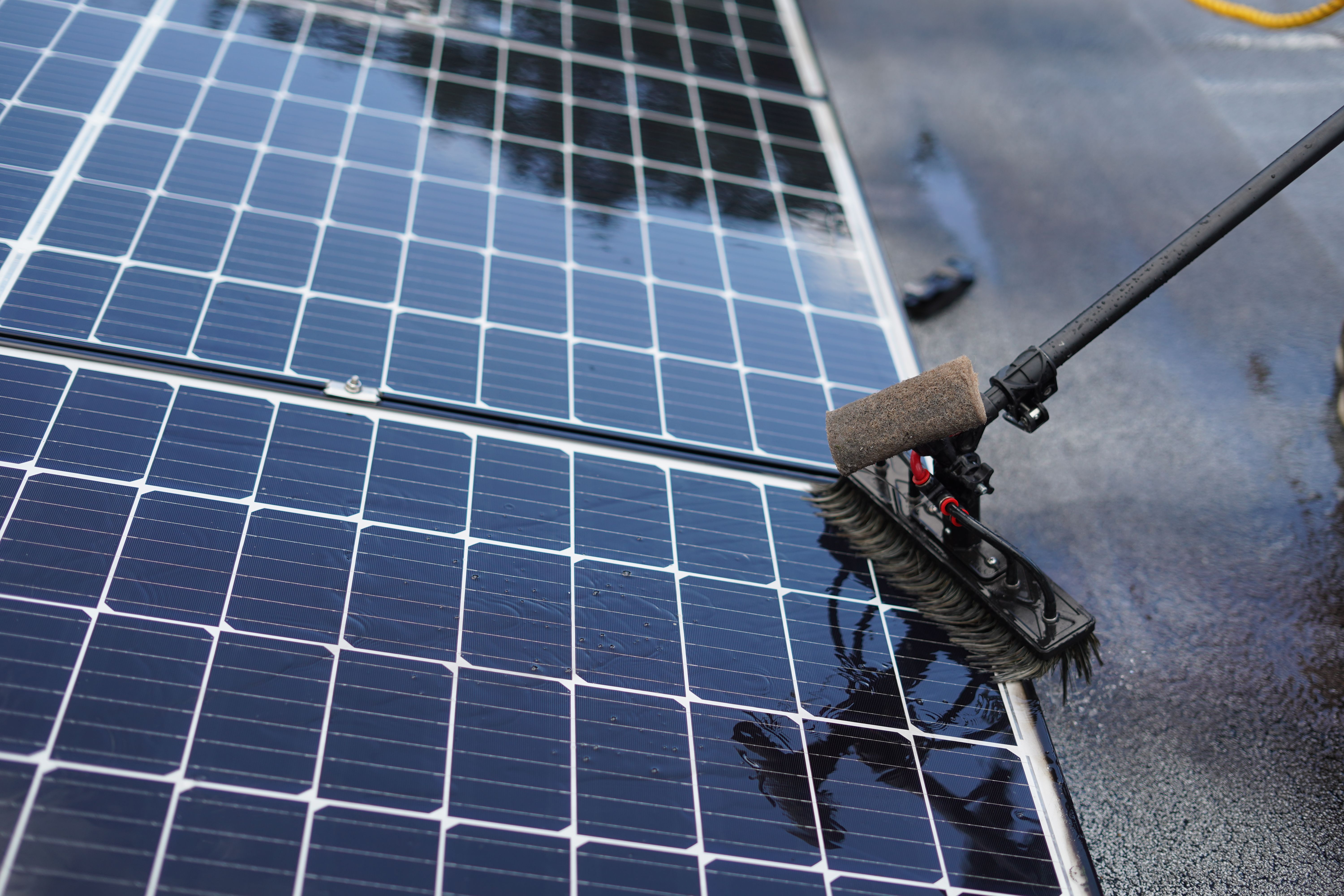 A cleaning tool with a sponge sweeps a solar panel to remove dirt.