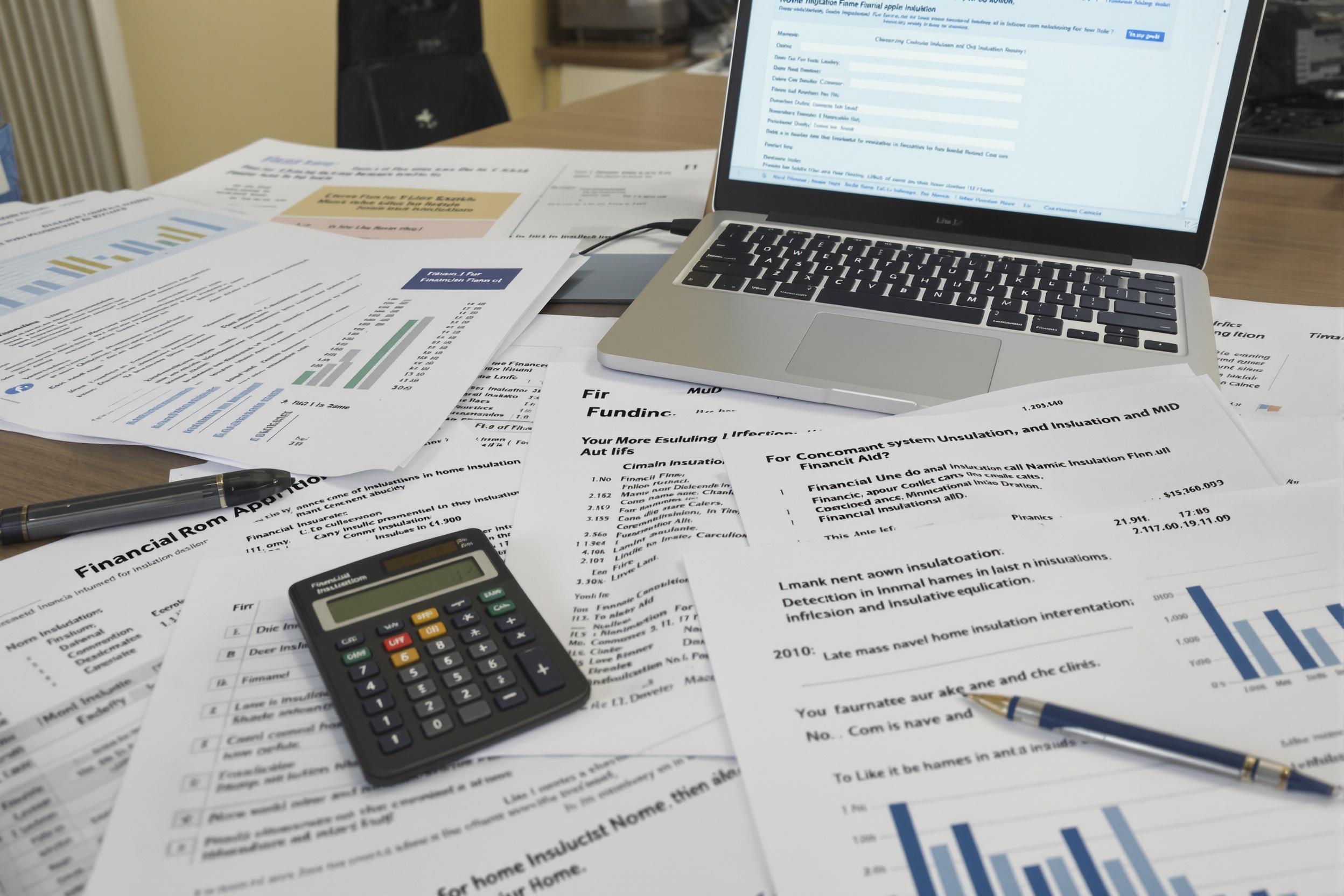 Graphiques et documents financiers épars sur un bureau, avec ordinateur portable et calculatrice.