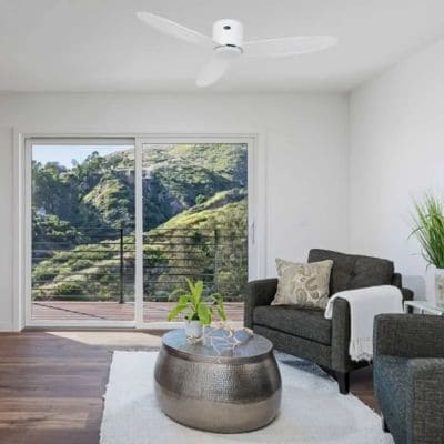 Ventilateur plafond blanc dans un salon lumineux, avec canapé gris, table basse et terrasse extérieure visible par la baie vitrée. choisir la bonne taille ventilateur plafond intégré naturellement.