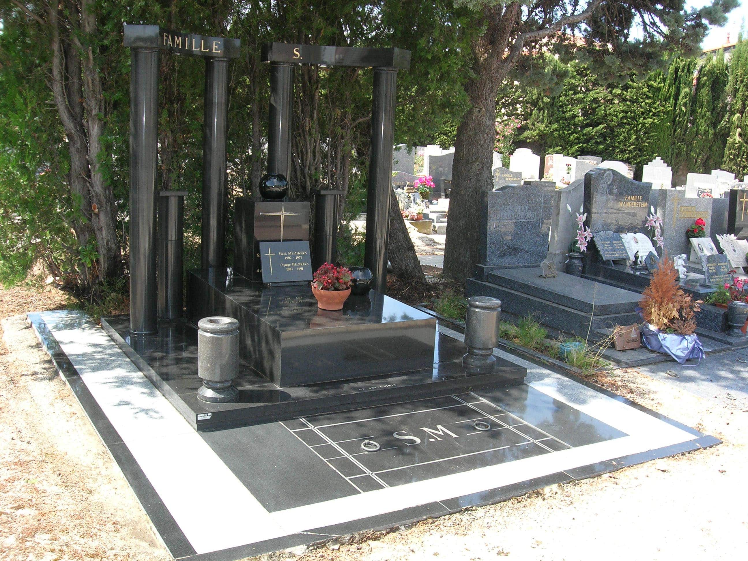 Une pierre tombale en marbre noir avec des fleurs se trouve dans un cimetière.