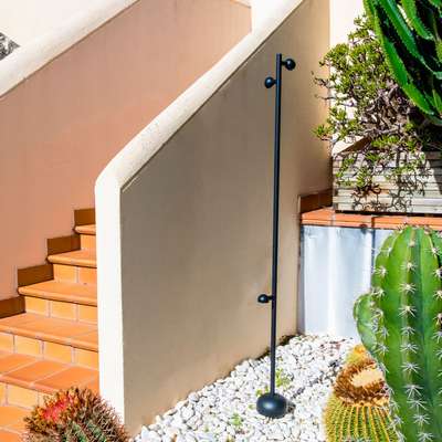 Lampadaire extérieur solaire noir posé près d’un escalier en façade, dans un jardin avec des cactus et gravier blanc.