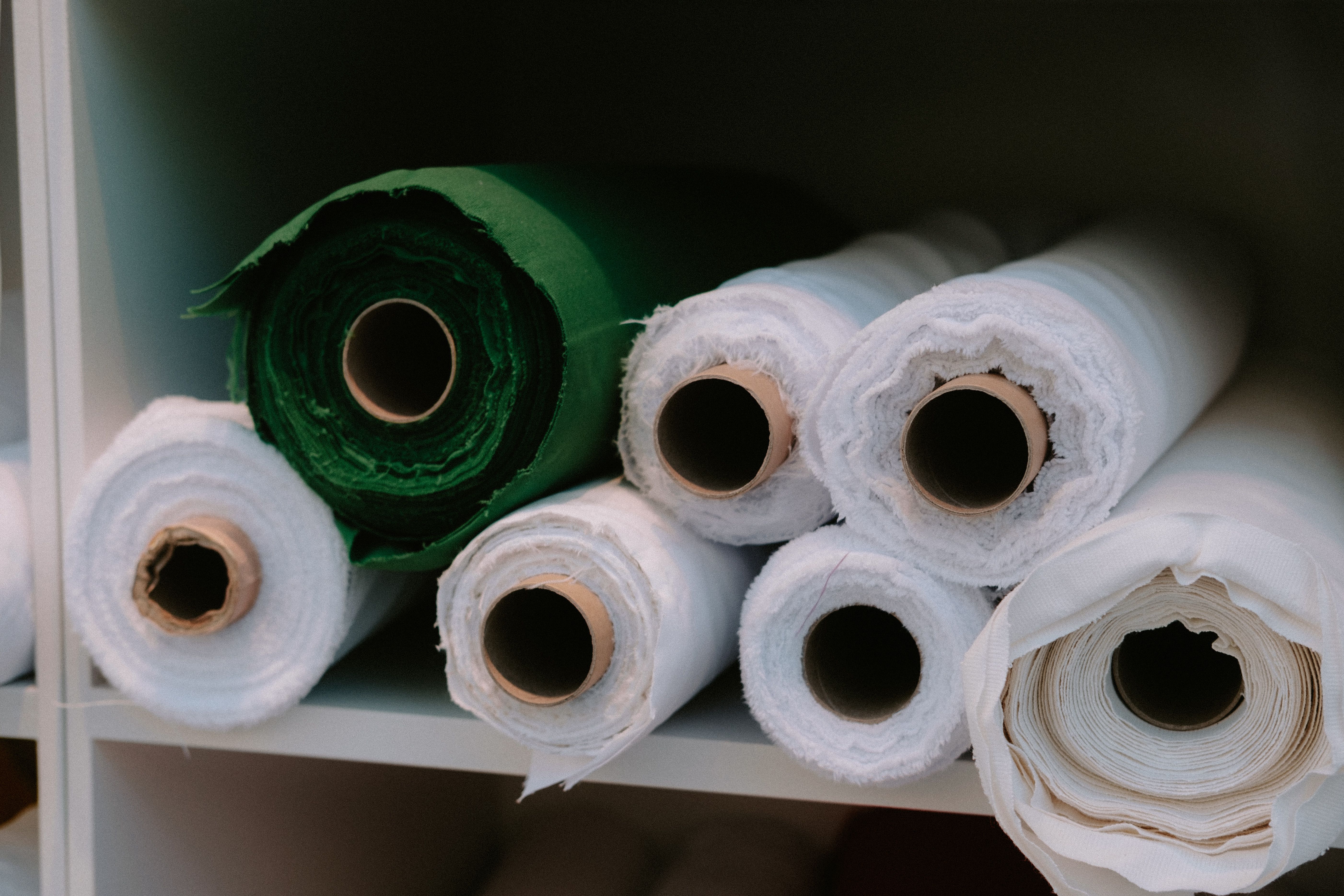 Rangements de rouleaux de tissu blancs et verts rangés sur des étagères d’atelier couture, parfait pour l’aménagement d’un atelier couture et le rangement des tissus