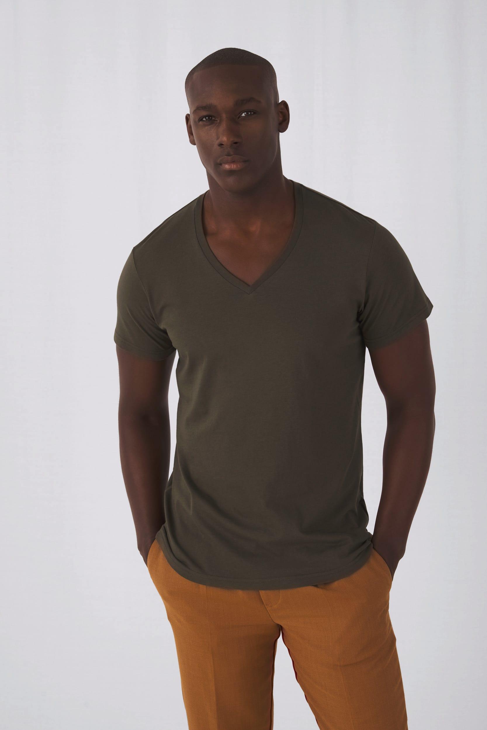 Homme africain debout portant un tee shirt olive à col V, pantalon orange, pose décontractée contre fond clair. tee shirt personnalisé livraison rapide suggéré.