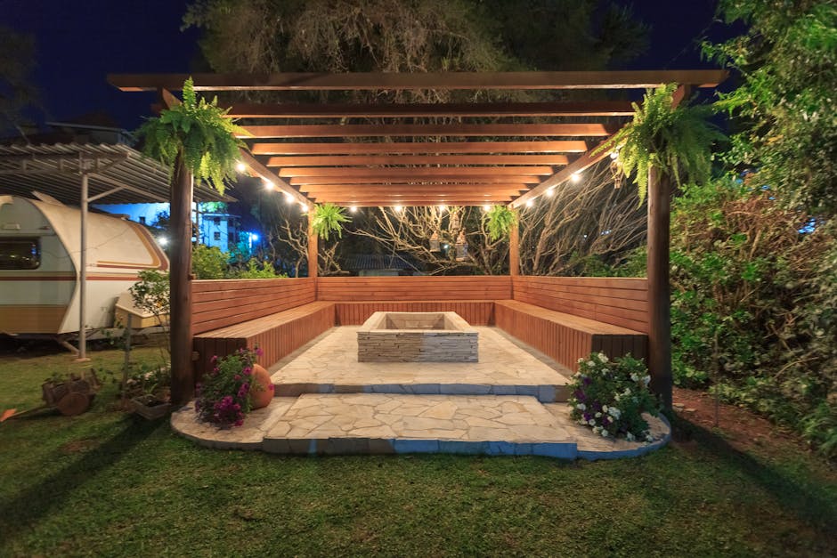 Kiosque en bois illuminé avec cheminée et bancs dans un jardin la nuit.