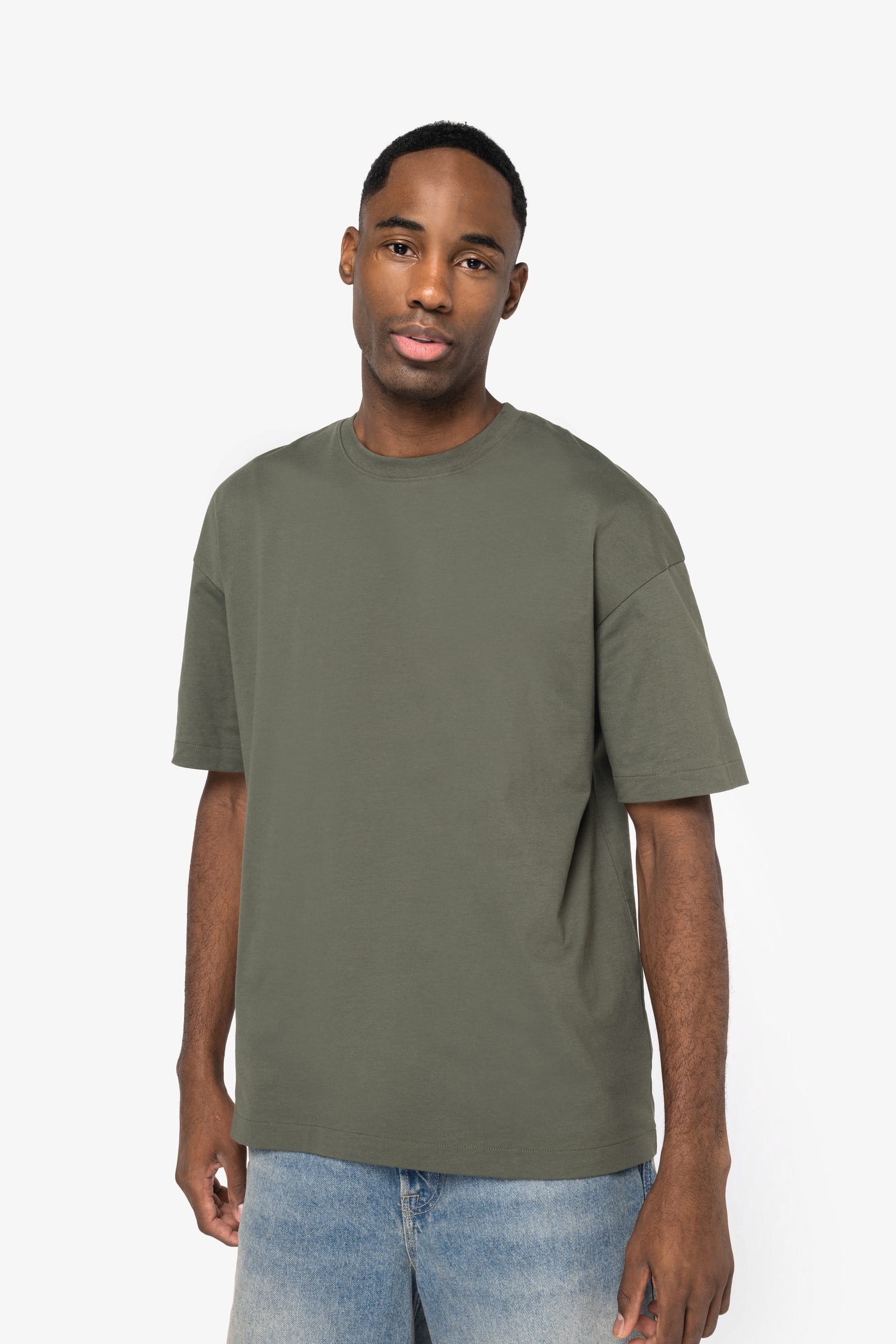 Homme portant un tee-shirt kaki ample, debout contre fond clair, jeans bleu décontracté. où personnaliser tee-shirt.
