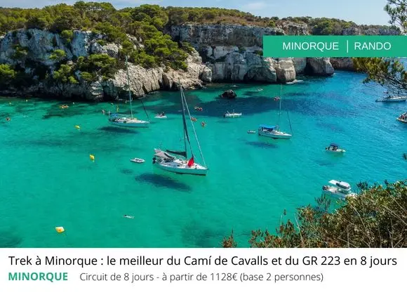 Vue d’une crique turquoise à Minorque avec bateaux amarrés; paysage côtier rocheux et végétation, texte superposé “MINORQUE | RAND0” sur l’image.
