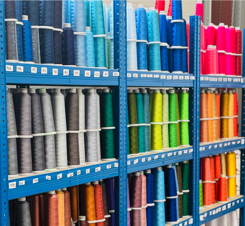 Fils de bobines de coutures multicolores rangés sur des étagères métalliques dans un atelier de textile.