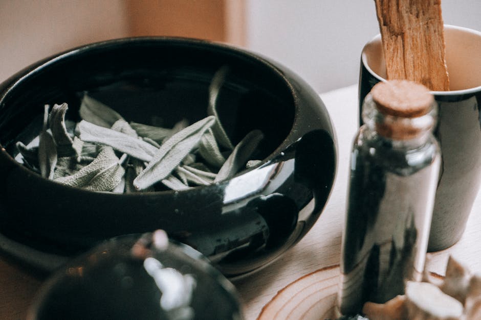 Un gros plan de feuilles de sauge dans un bol en céramique, accompagné de flacons d'aromates, évoquant un cadre naturel et paisible.