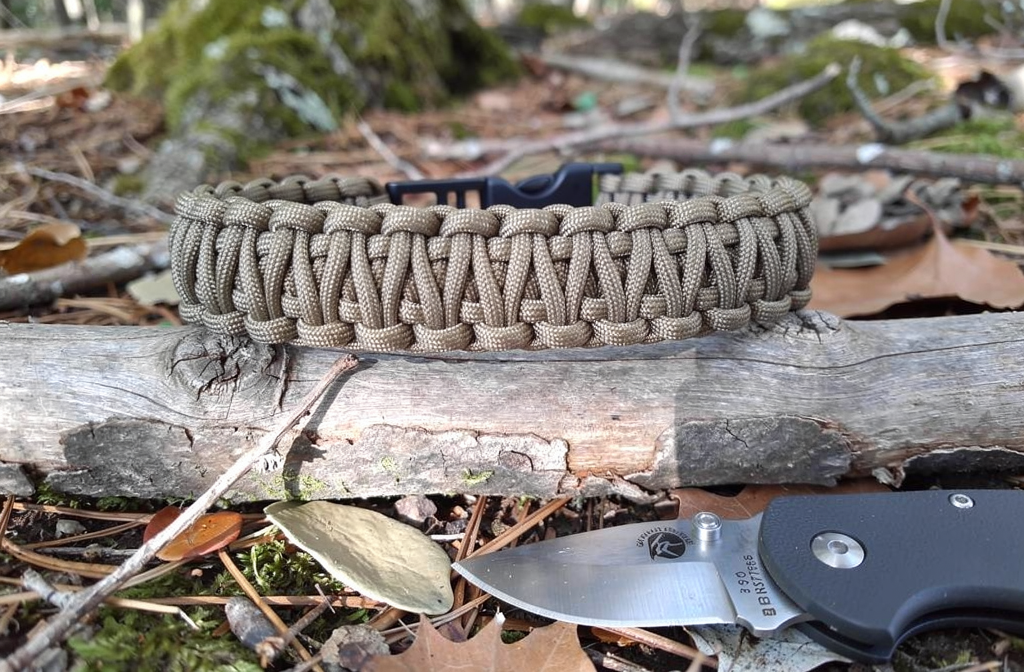 Bracelet en paracorde tressé posé sur une bûche en forêt pour le bushcraft