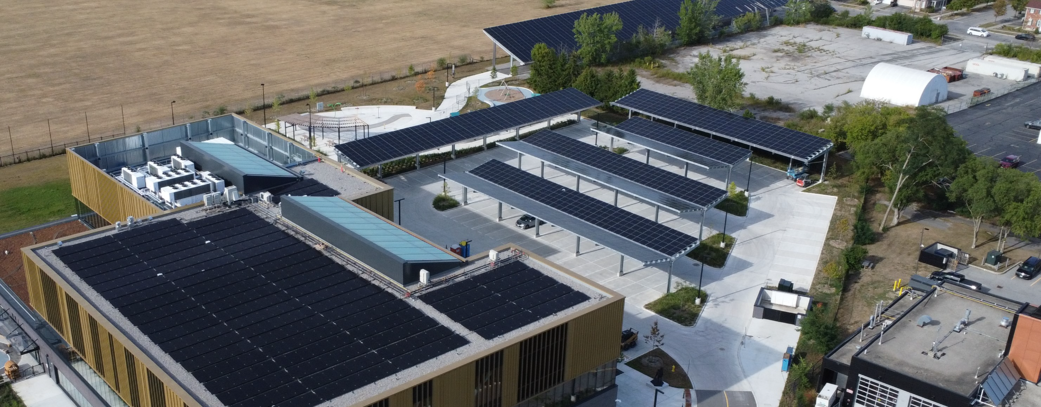 Aerial view of a commercial complex with multiple solar panel canopies over parking areas and adjacent building rooftops in Toronto, showcasing a solar installation on flat roofs and shaded parking.